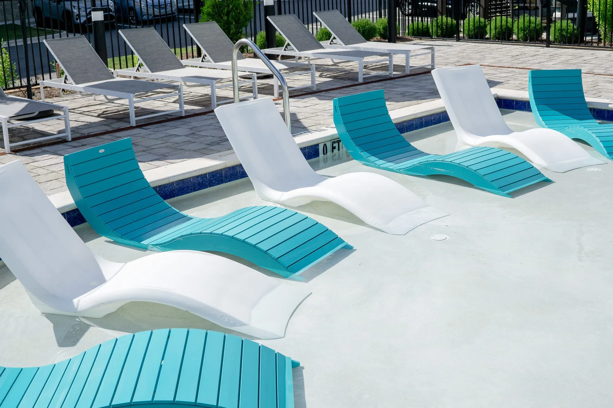 Multifamily community pool with alternating white and teal loungers set in the shallow sun shelf