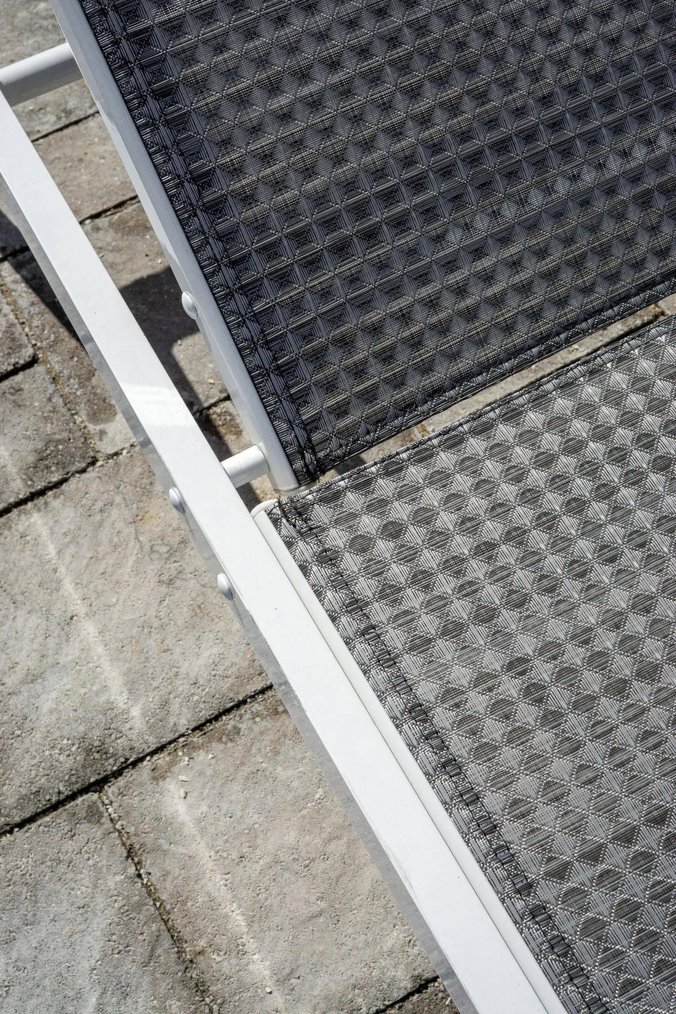 Multifamily community exterior detail: white-framed mesh chaise on stone pavers, seen from above
