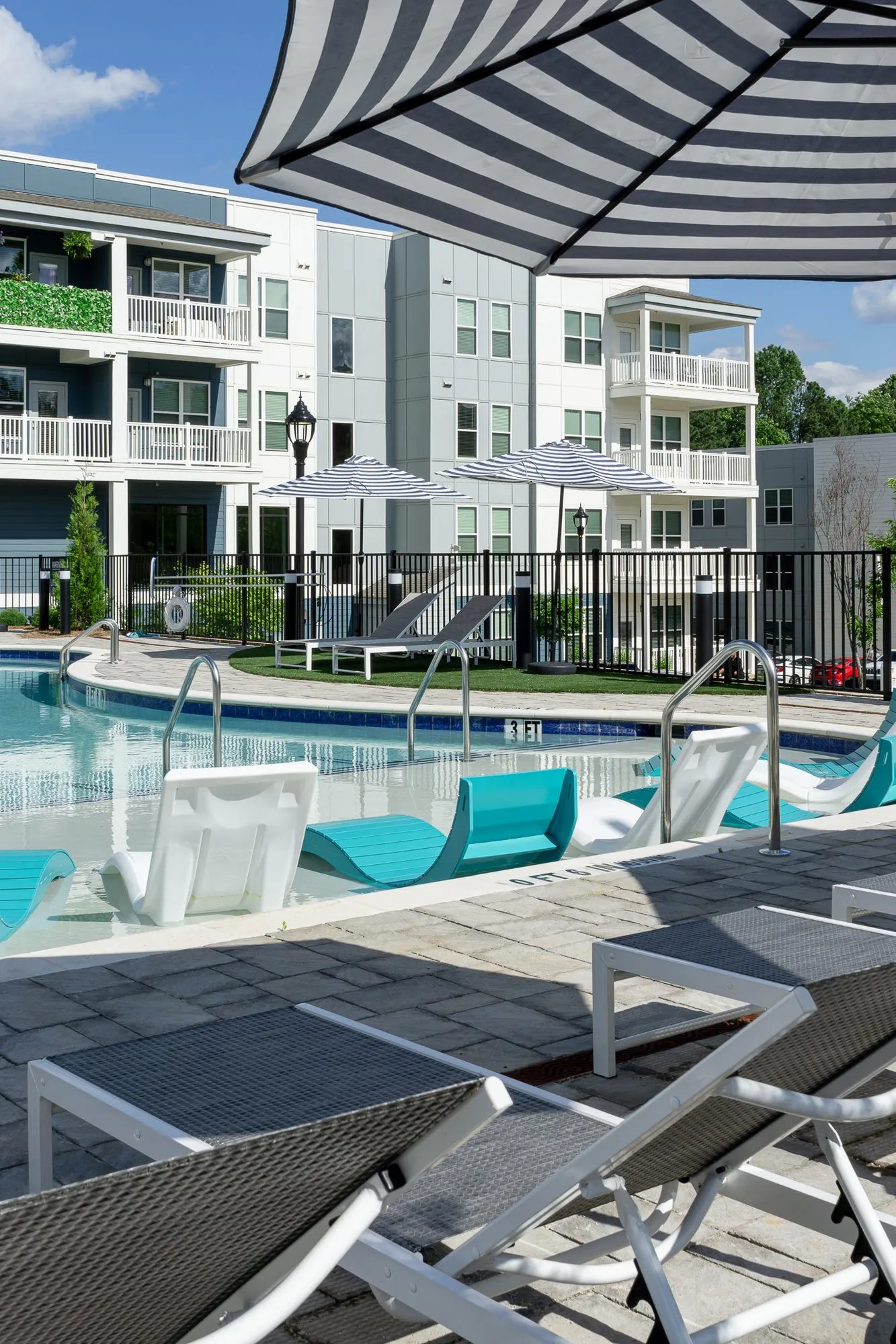 Multifamily community pool deck of chaises and in-water loungers toward the apartments
