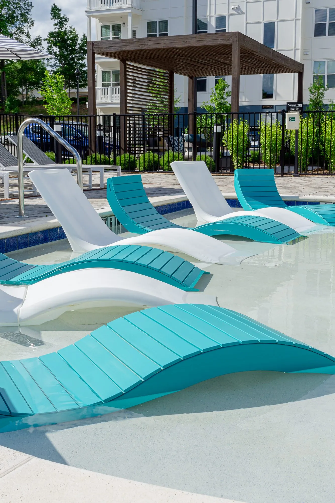 Multifamily community pool with a teal lounger in front of white and teal loungers on the sun shelf