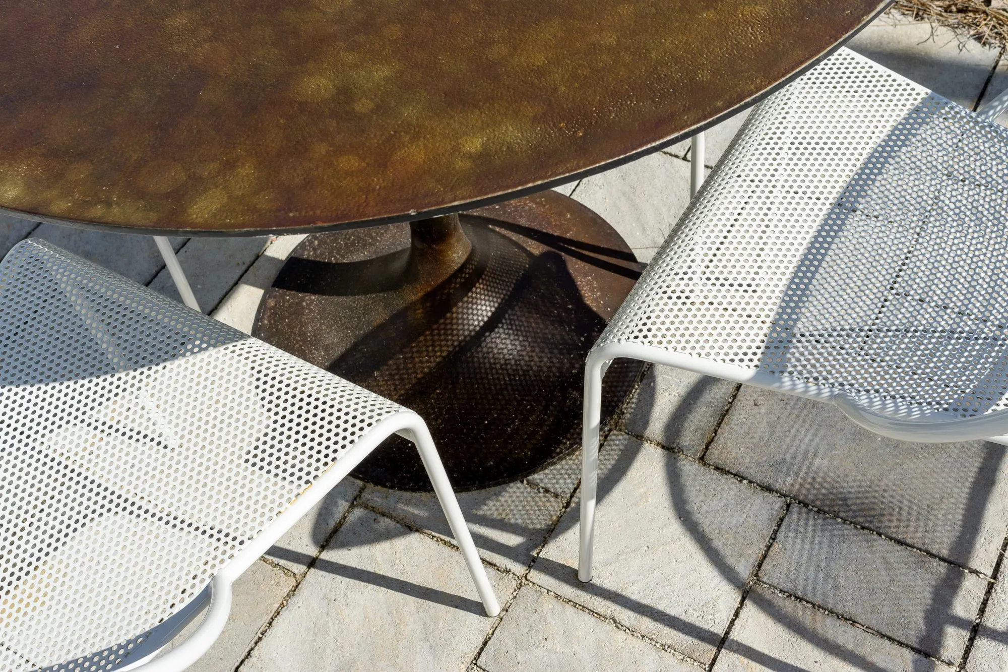 Multifamily community exterior detail: white perforated metal chairs beside a bronze patio table