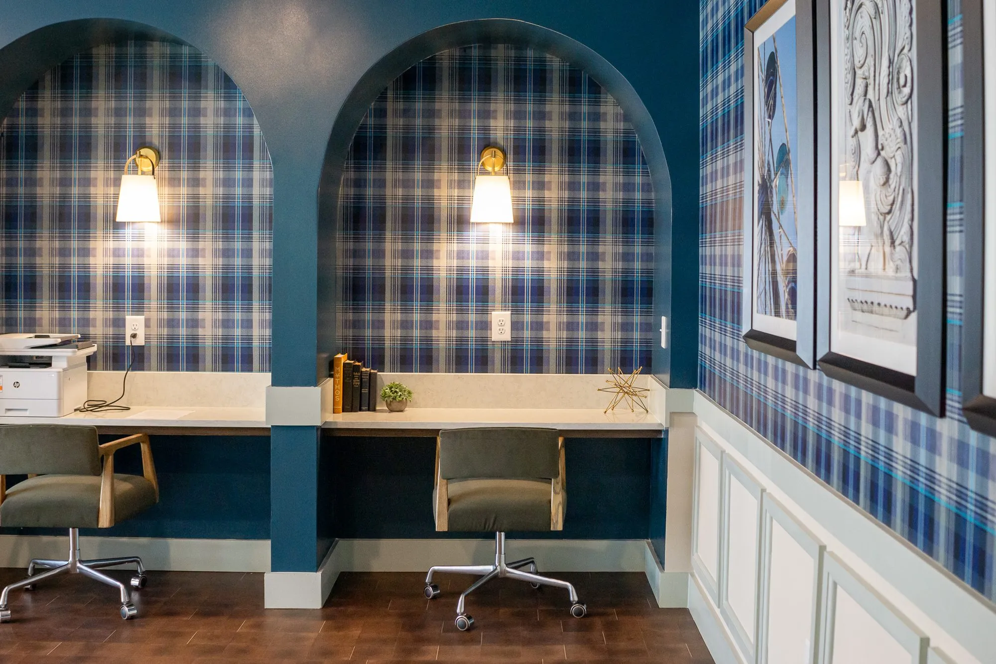 Multifamily amenity arched desk niches in dark teal lined with plaid wallpaper, brass sconces and green chairs, framed prints