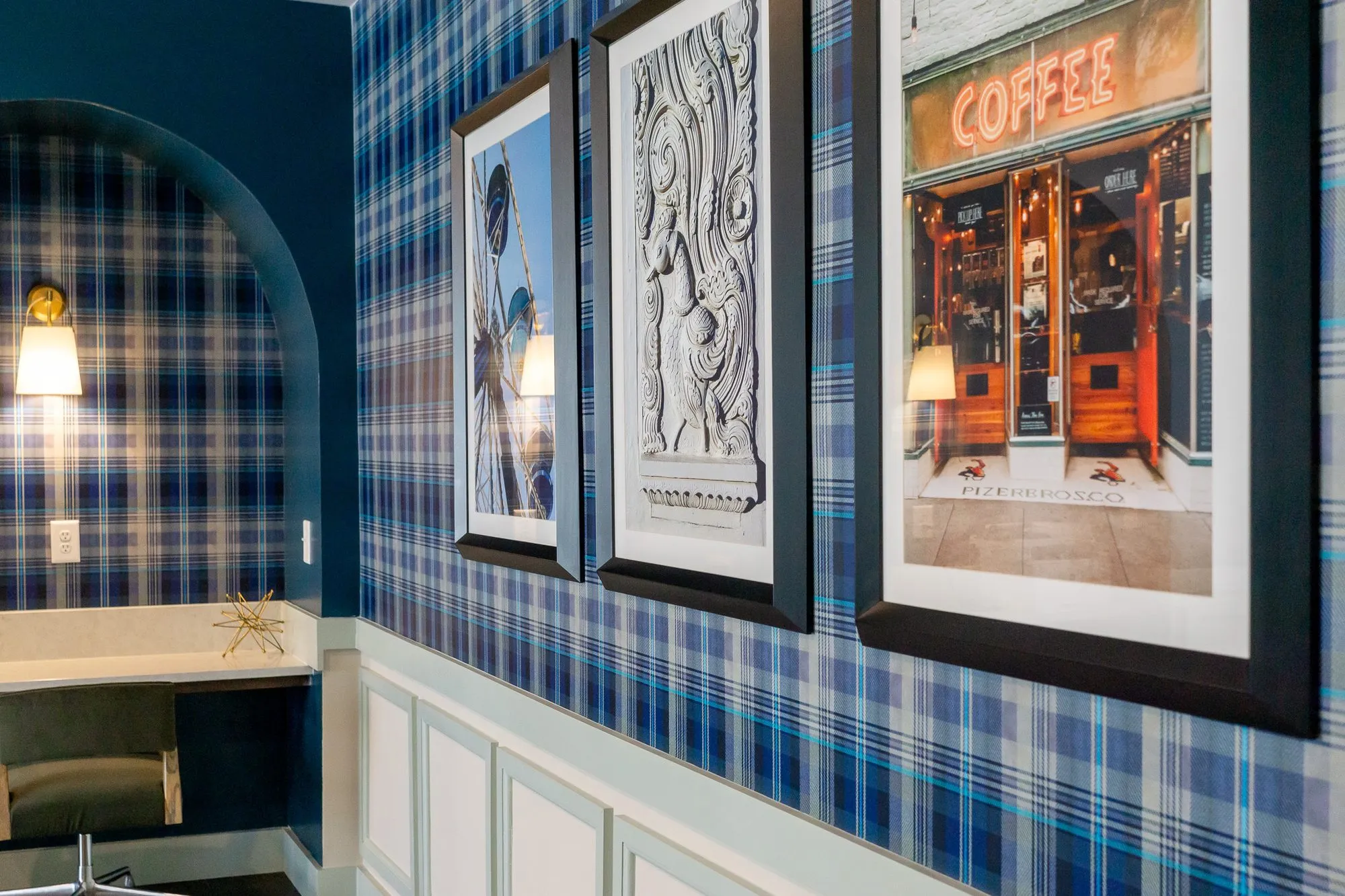 Multifamily amenity interior detail: framed prints including a lit coffee shop facade beside an arched plaid desk niche