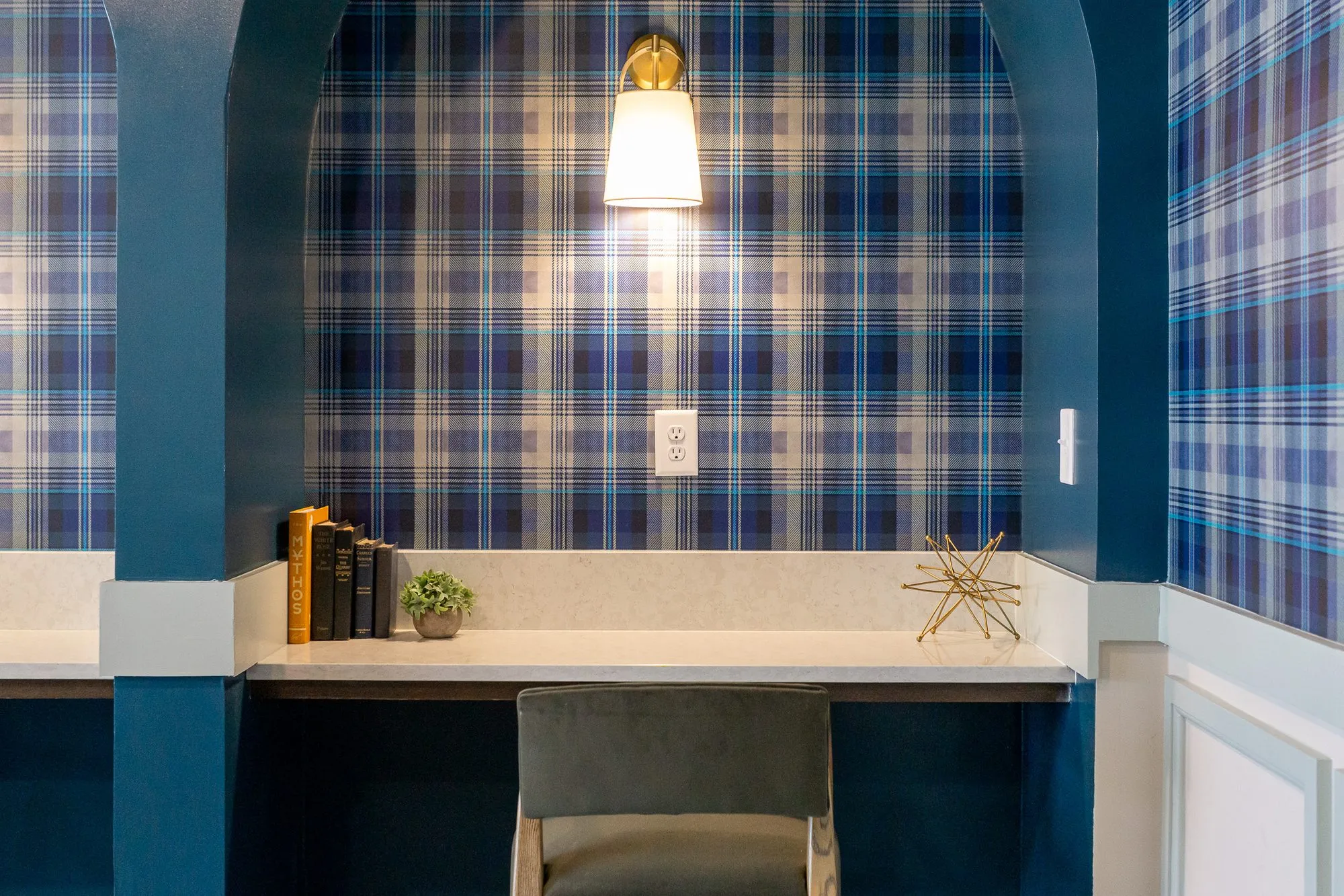 Multifamily amenity desk niche lined in plaid with a brass sconce, books and a green chair