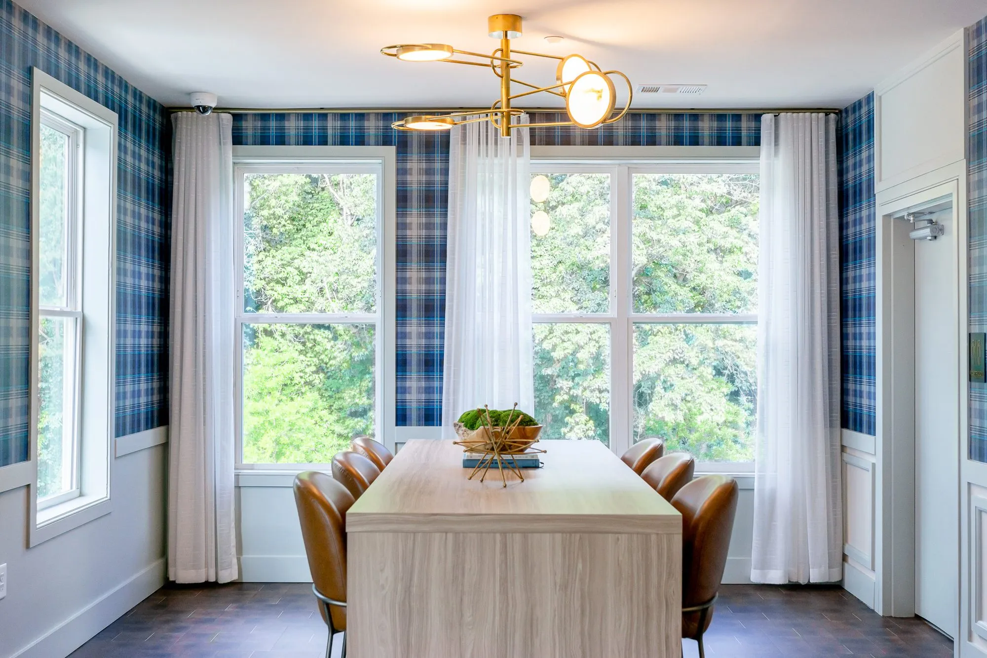Multifamily amenity conference room with plaid walls, a pale wood table and cognac chairs under a brass disc fixture