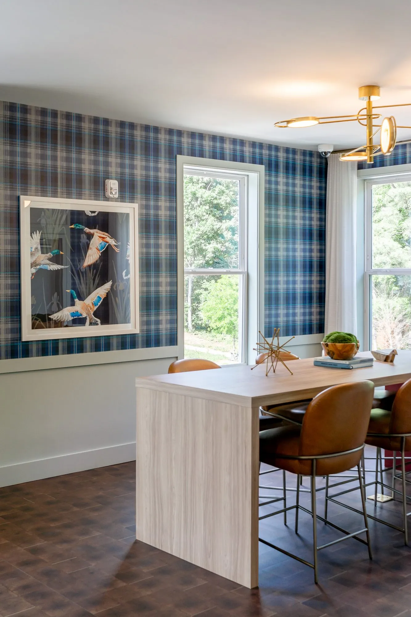 Multifamily amenity conference room with cognac chairs at the table below a framed duck print on plaid wallpaper