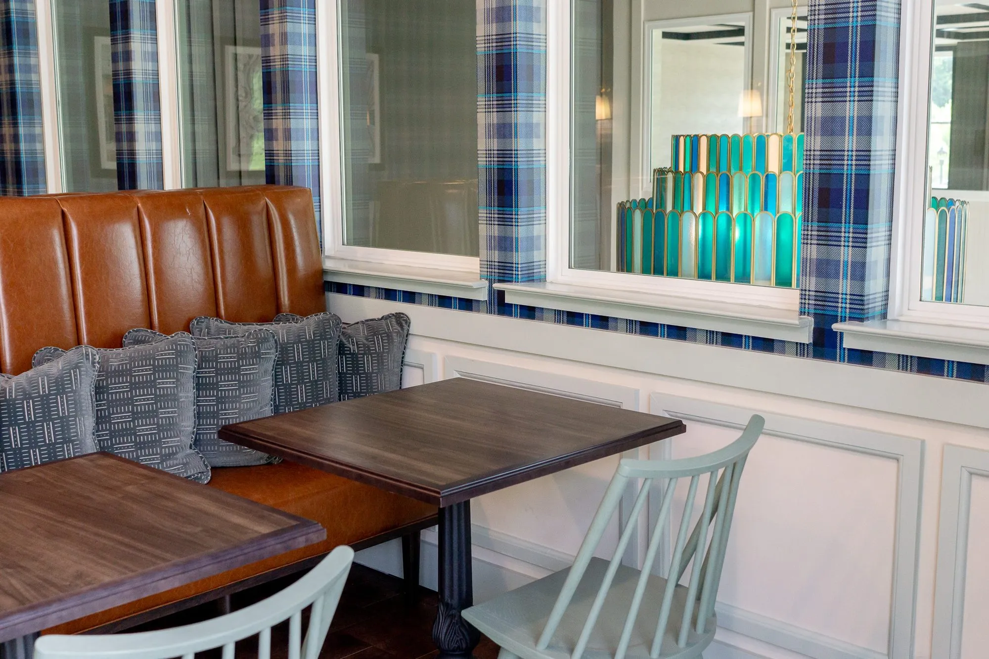 Multifamily amenity cafe with a cognac banquette and grey pillows under an interior window showing the glass chandelier