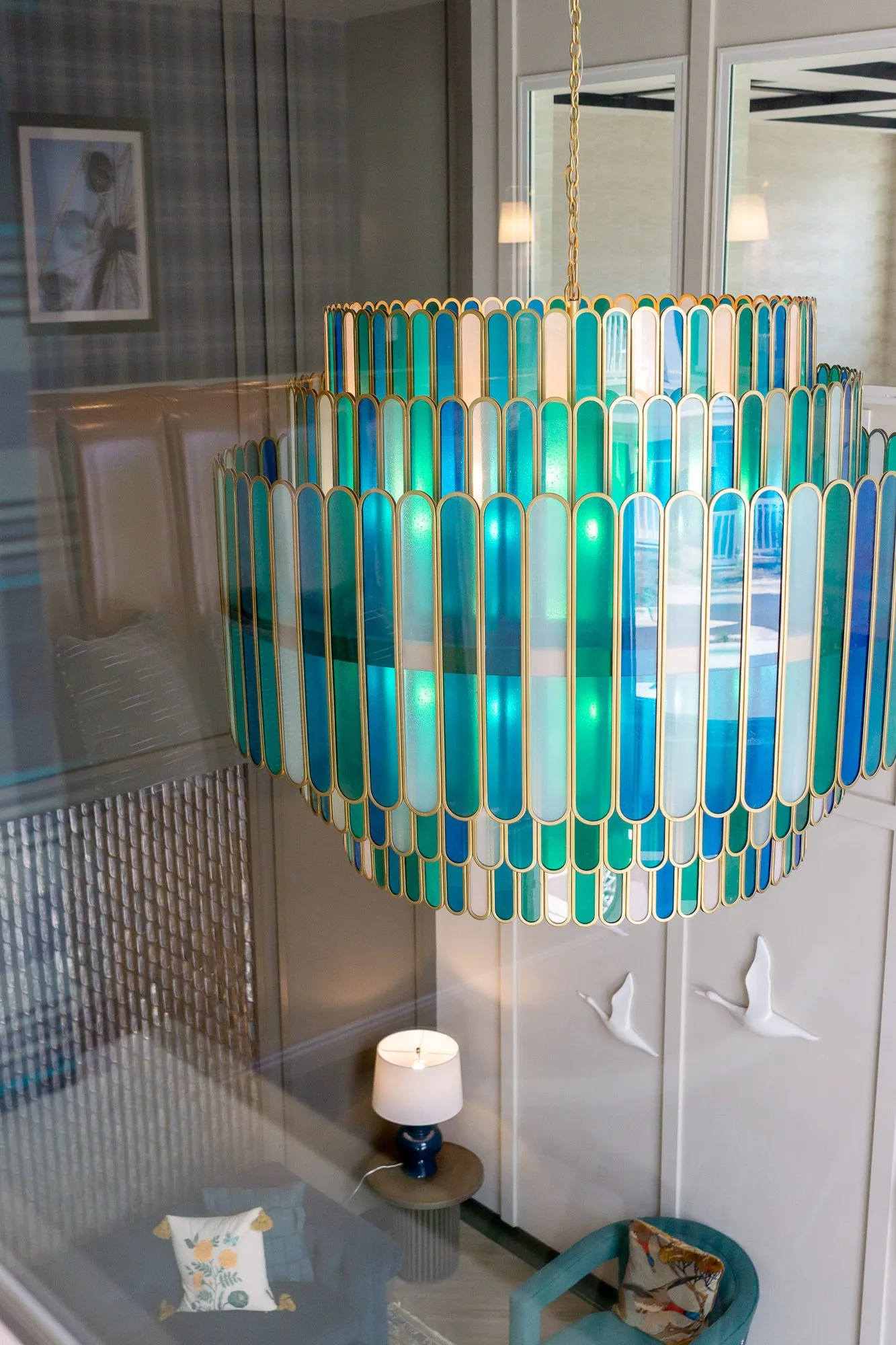 Multifamily amenity lobby lounge below the tiered glass chandelier, seen through an interior window