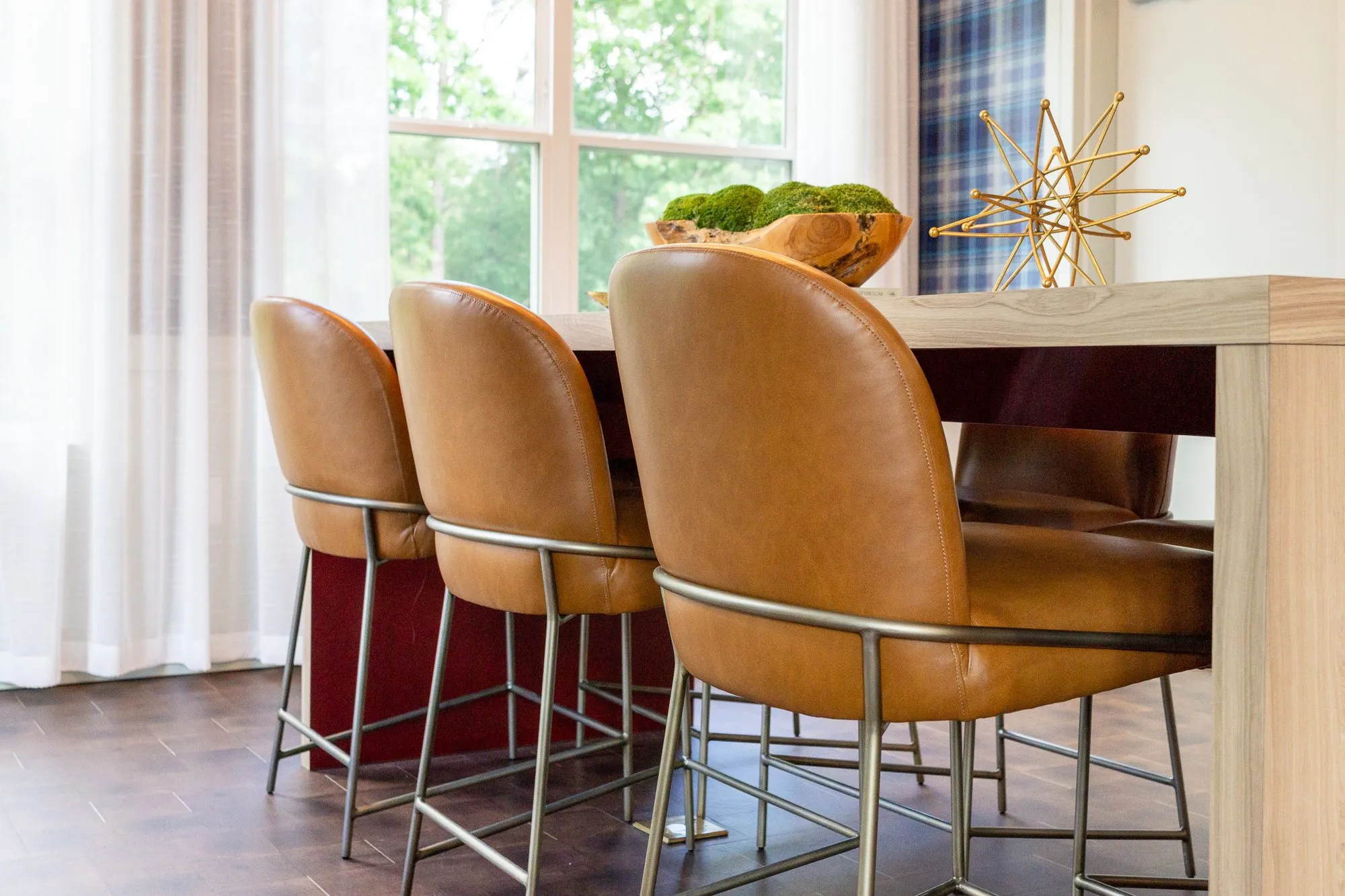 Multifamily amenity conference room with cognac leather chairs along a pale wood table, a moss bowl and brass star