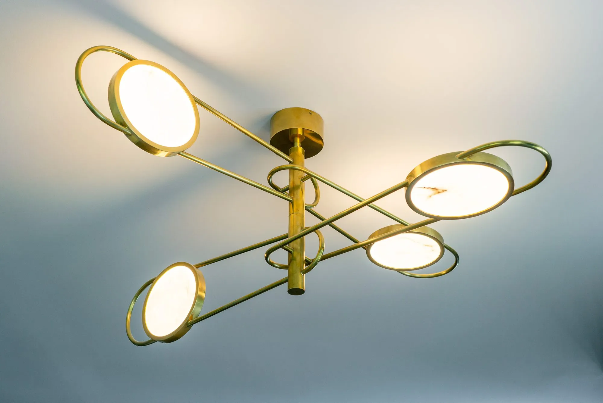 Multifamily amenity conference room light, a brass fixture of four ring-framed glowing discs on crossed arms