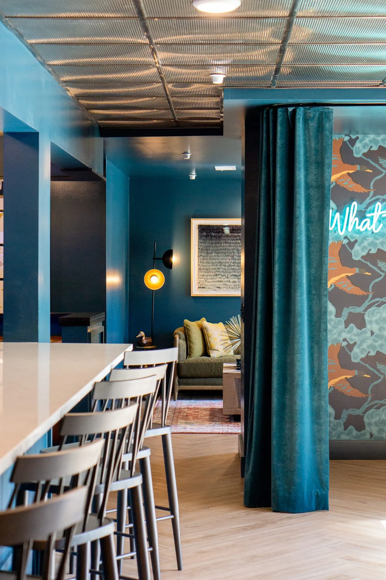 Multifamily amenity bar with wood stools leading to a teal velvet curtain and a lounge beyond