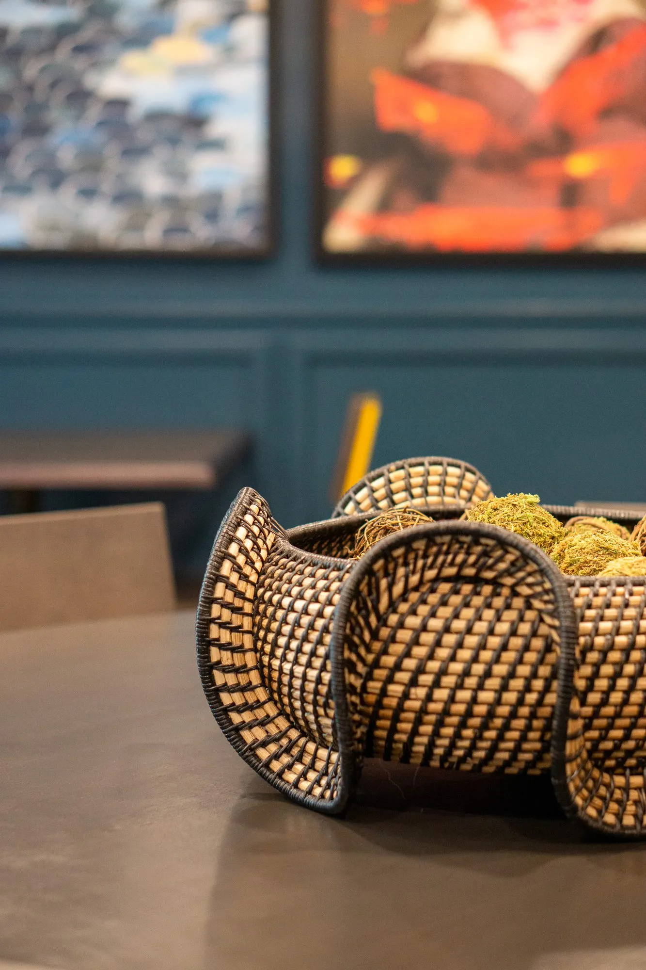 Multifamily amenity interior detail: woven basket bowl on a dark table, framed artworks on teal panelling behind