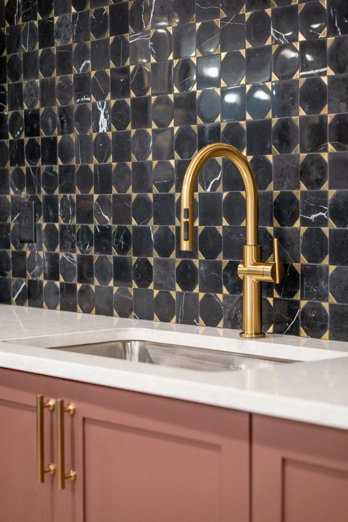 Multifamily amenity bar with a black and white marble mosaic backsplash behind a brass faucet over mauve cabinets