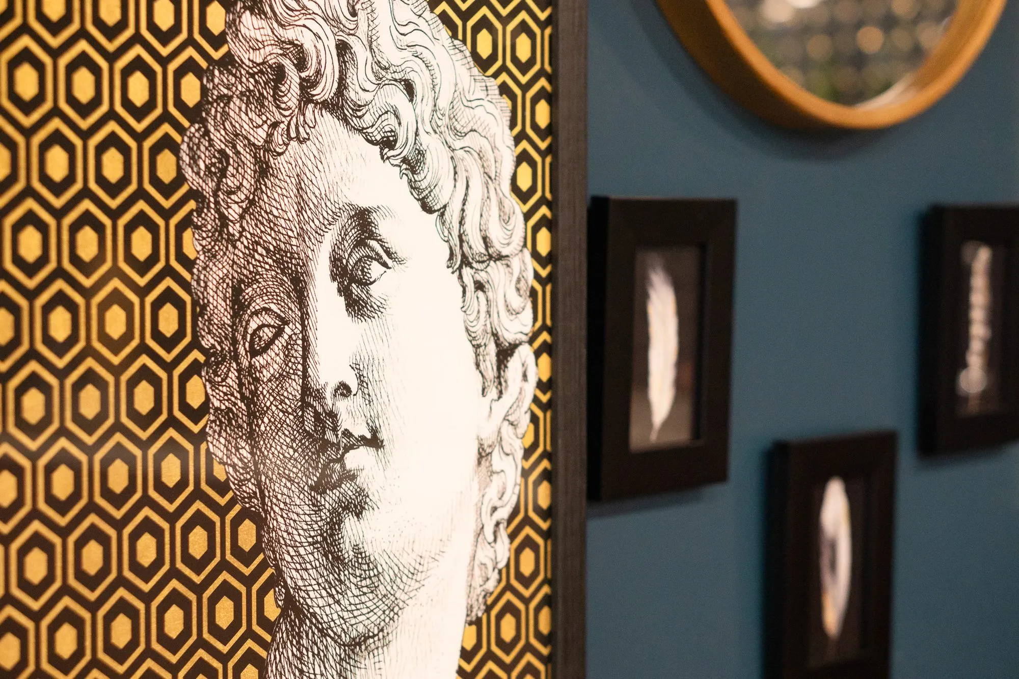 Multifamily amenity gallery wall with a classical bust print on gold hexagons beside small framed photographs on teal