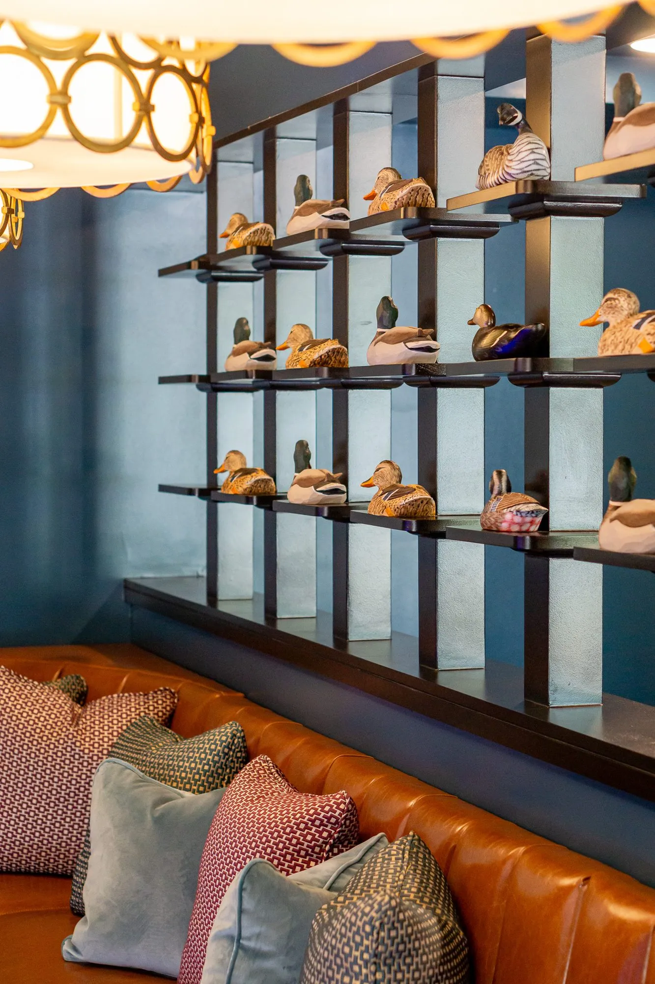Multifamily amenity bowling lounge with carved duck decoys on dark shelving above a cognac banquette