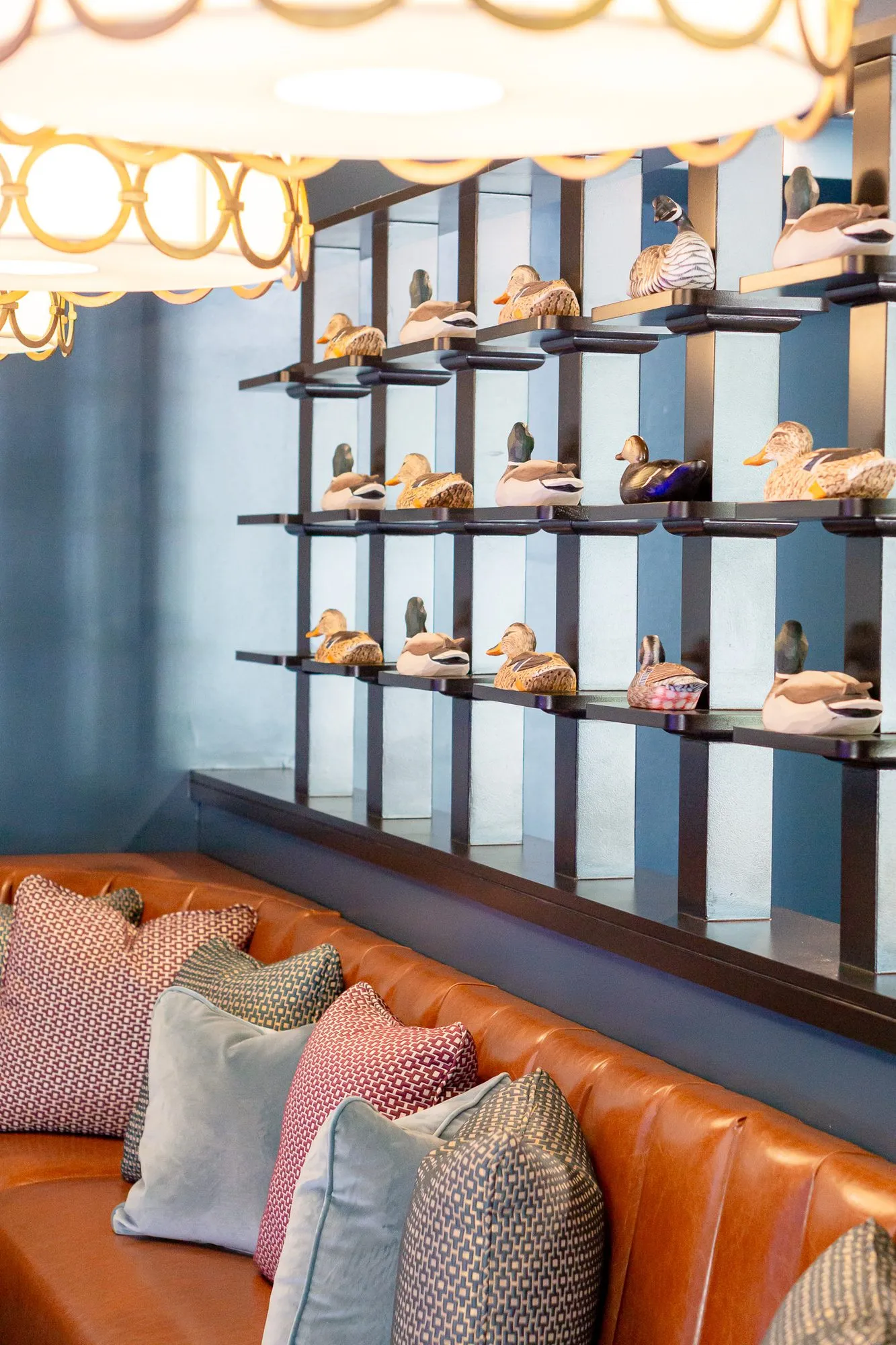 Multifamily amenity bowling lounge with a ring-pattern drum pendant above shelves of duck decoys and a leather banquette