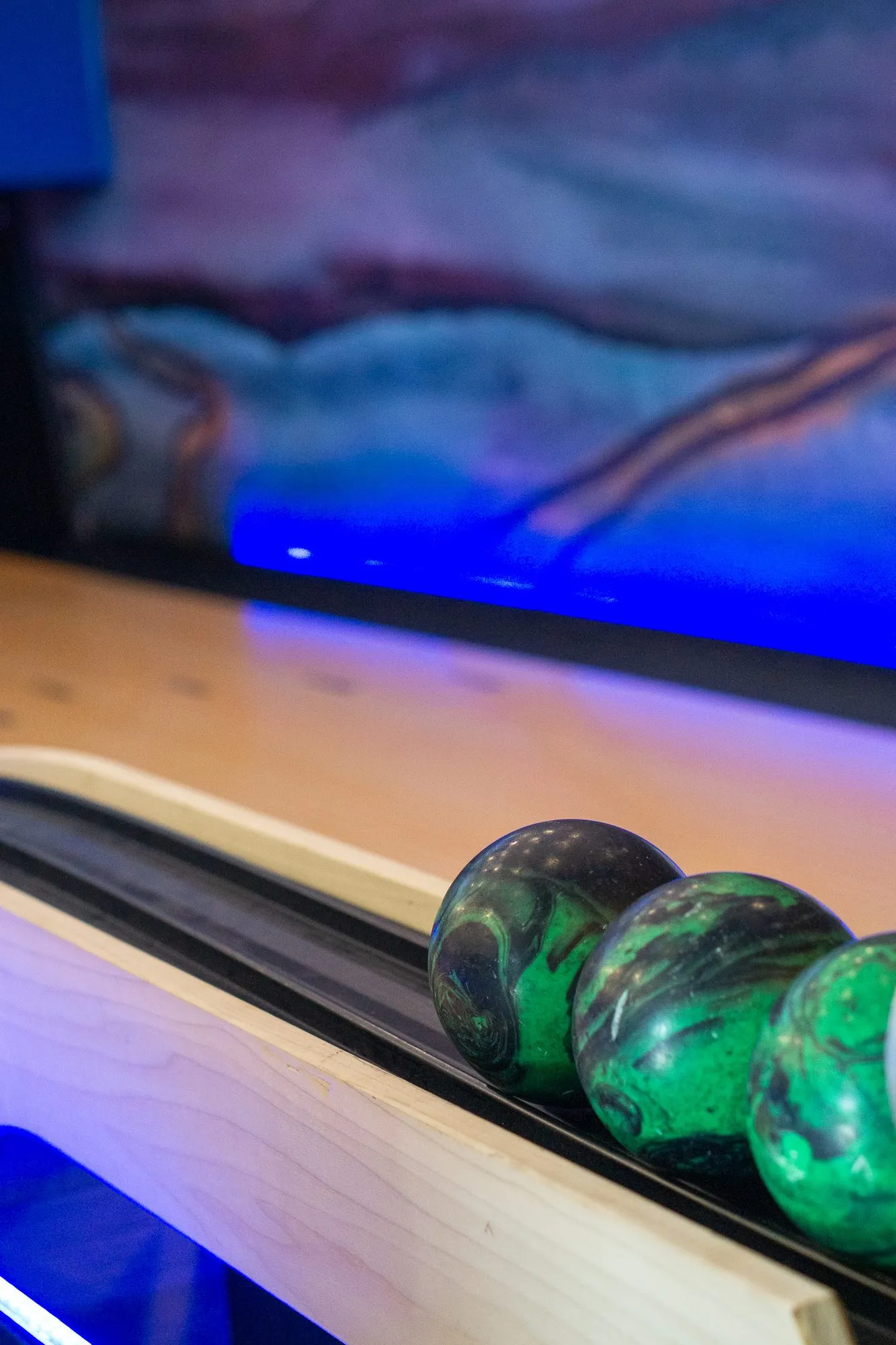 Multifamily amenity duckpin bowling alley with swirled green balls in the ball return beside a lit lane