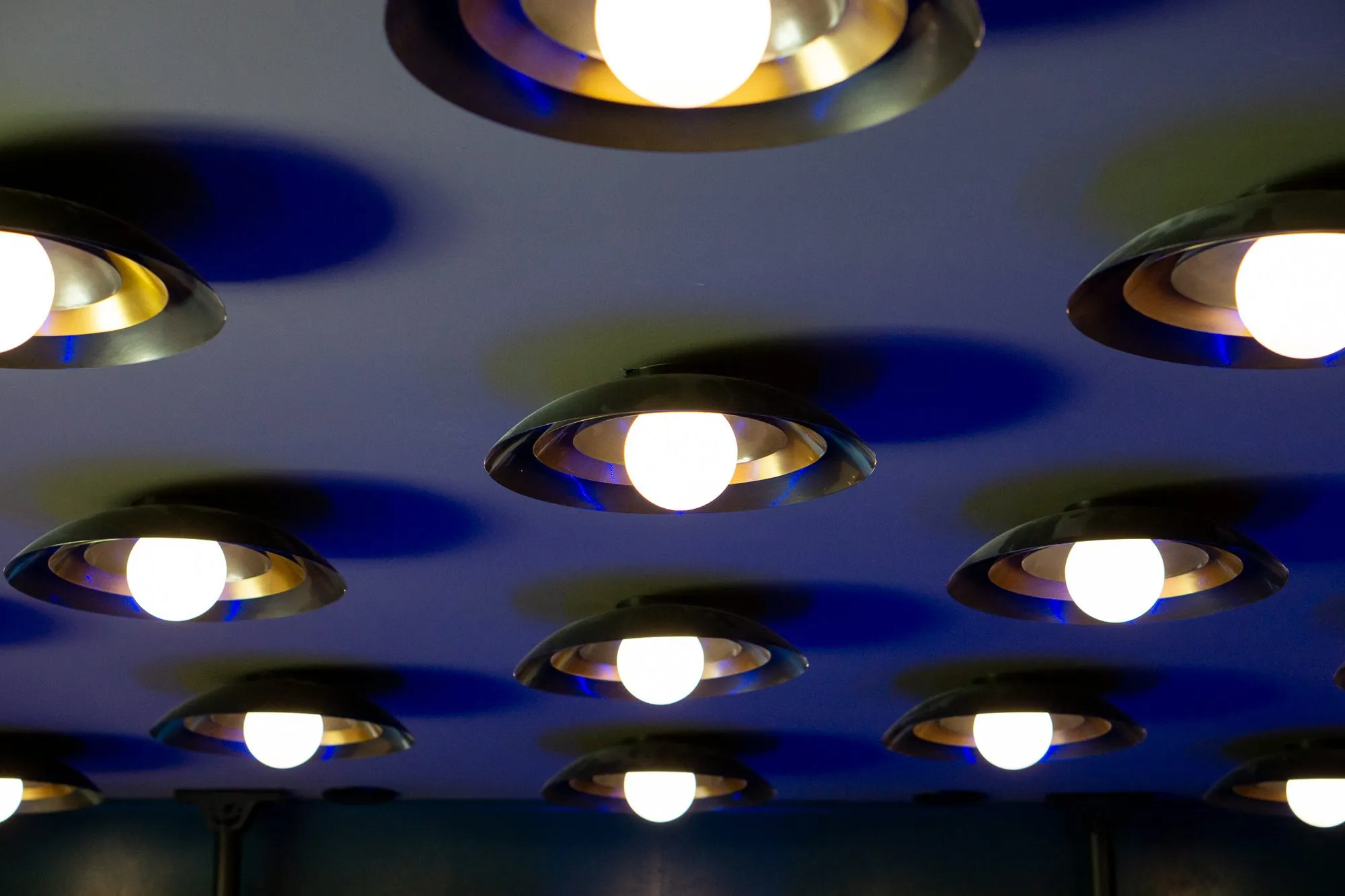 Multifamily amenity interior detail: rows of brass dome lights with bare bulbs on a blue ceiling