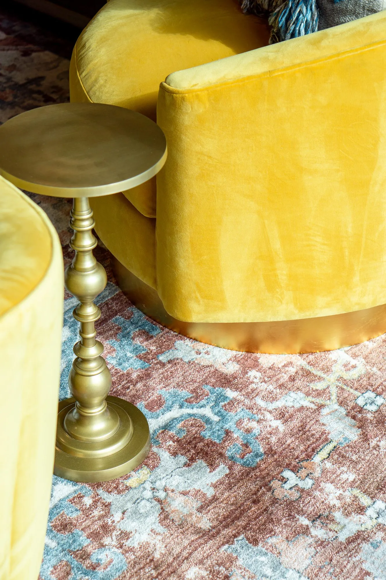 Multifamily interior detail: brass side table beside a yellow velvet chair on a faded rug