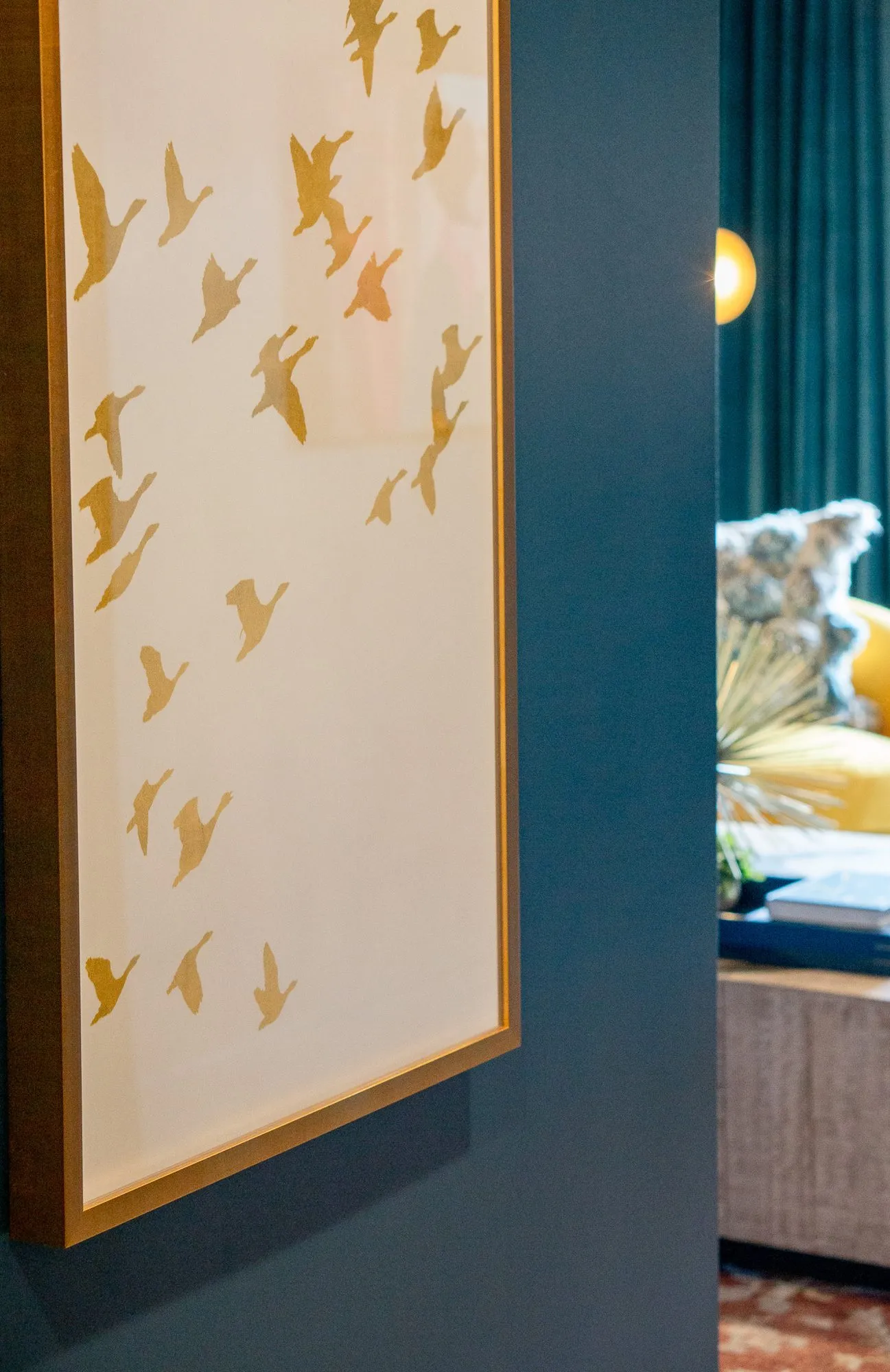 Multifamily interior detail: framed artwork of gold birds in flight on cream against a dark teal wall