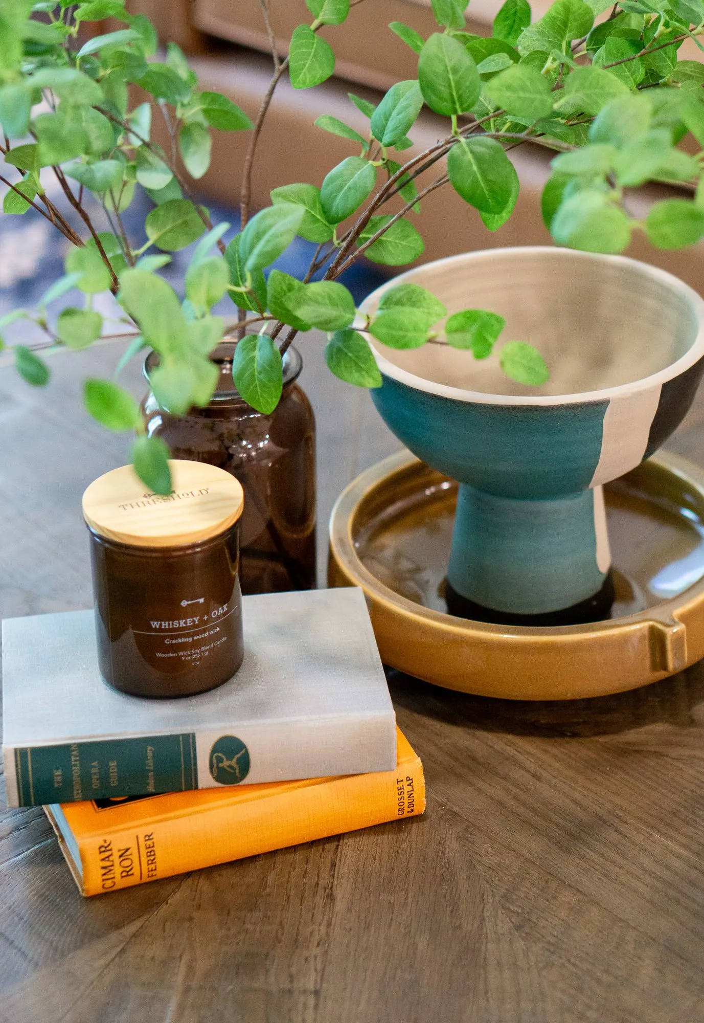 Multifamily apartment model living room coffee table with a candle, stacked books, a teal pedestal bowl and greenery