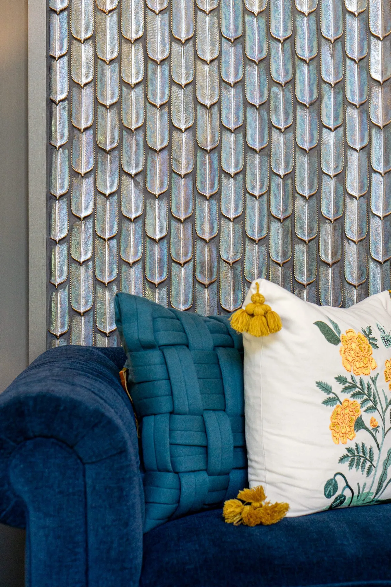 Multifamily amenity lobby lounge with a navy tufted sofa, teal woven and floral pillows against a feather tile panel