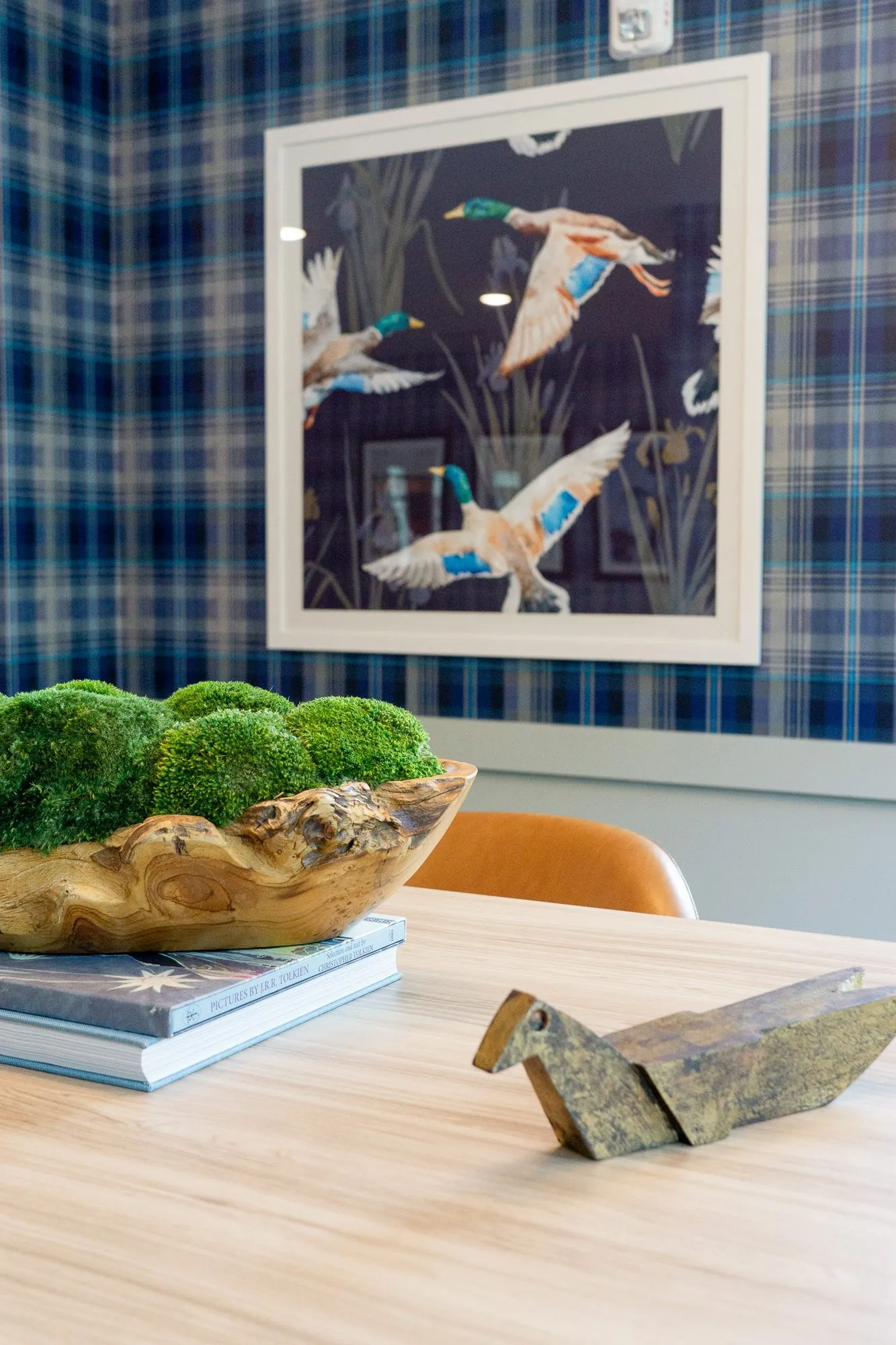 Multifamily amenity interior detail: moss bowl and brass bird on a table below a framed mallard print on plaid