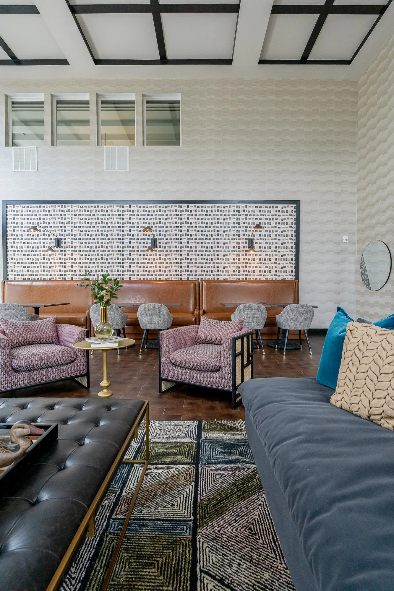 Multifamily amenity clubroom with a navy sofa and leather ottoman leading to pink chairs and leather booths