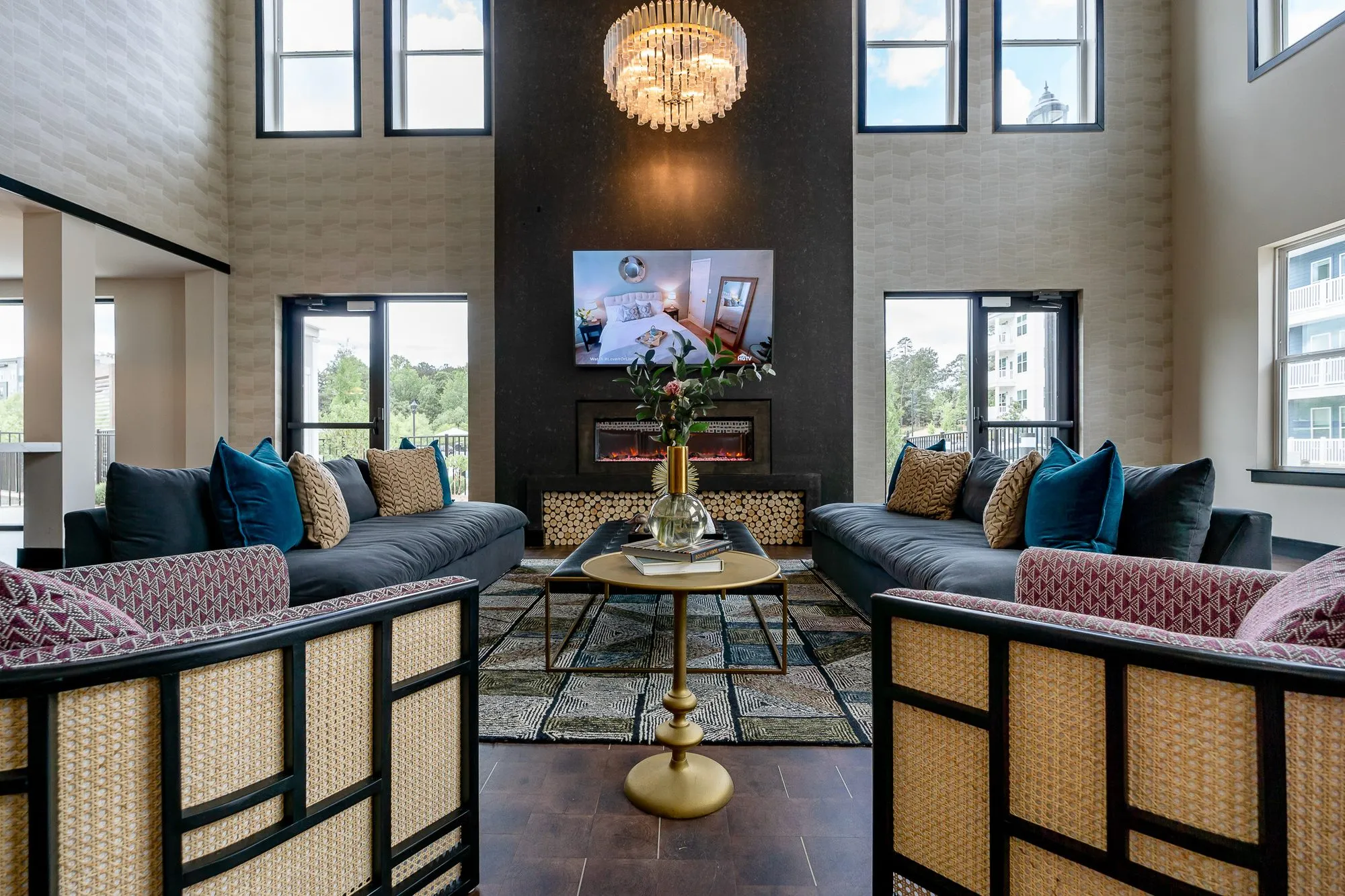 Multifamily amenity fireplace lounge with pink cane chairs and navy sofas under a crystal chandelier
