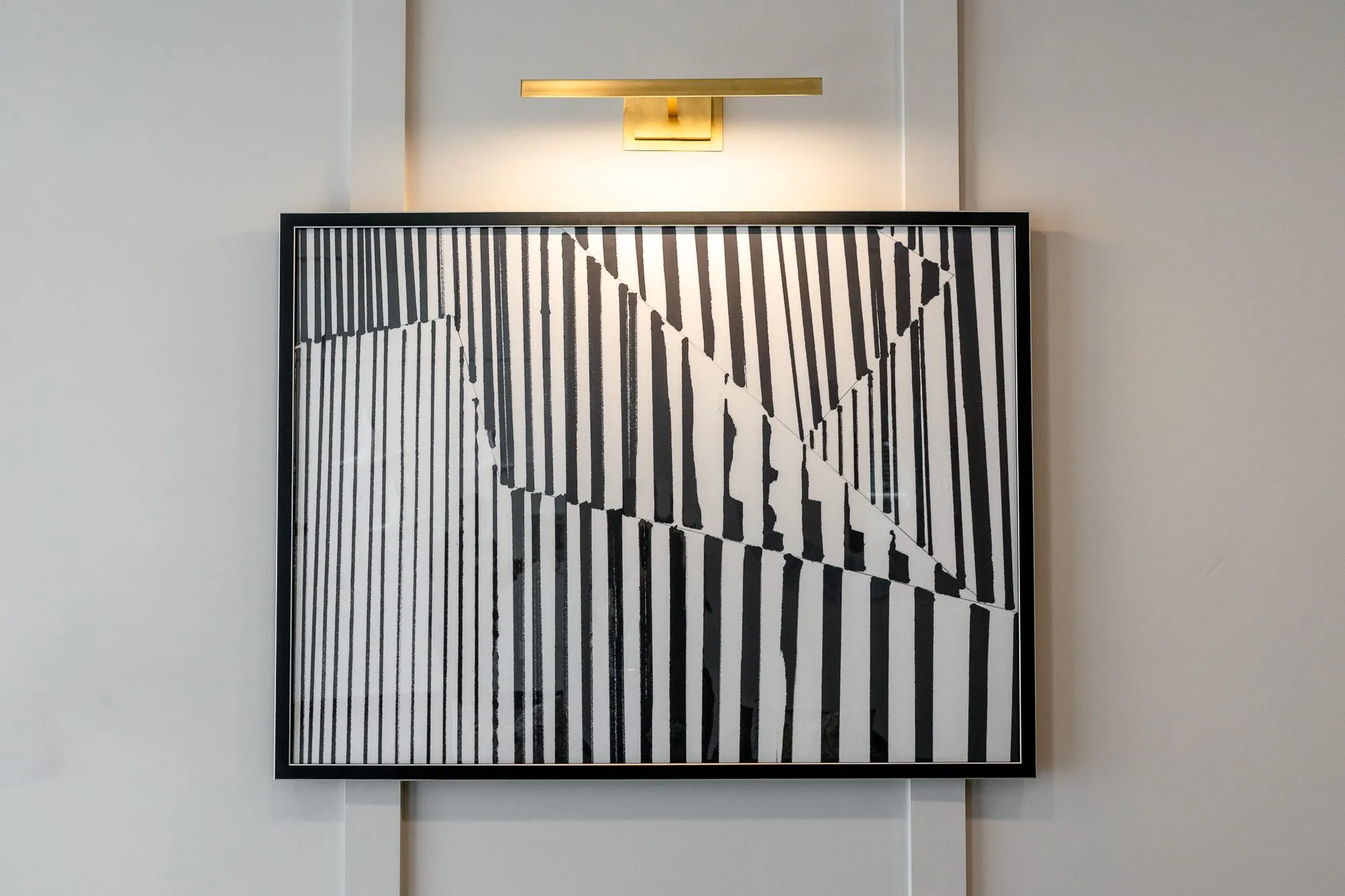 Multifamily amenity leasing area artwork, a black and white stripe abstract under a brass picture light on white panelling
