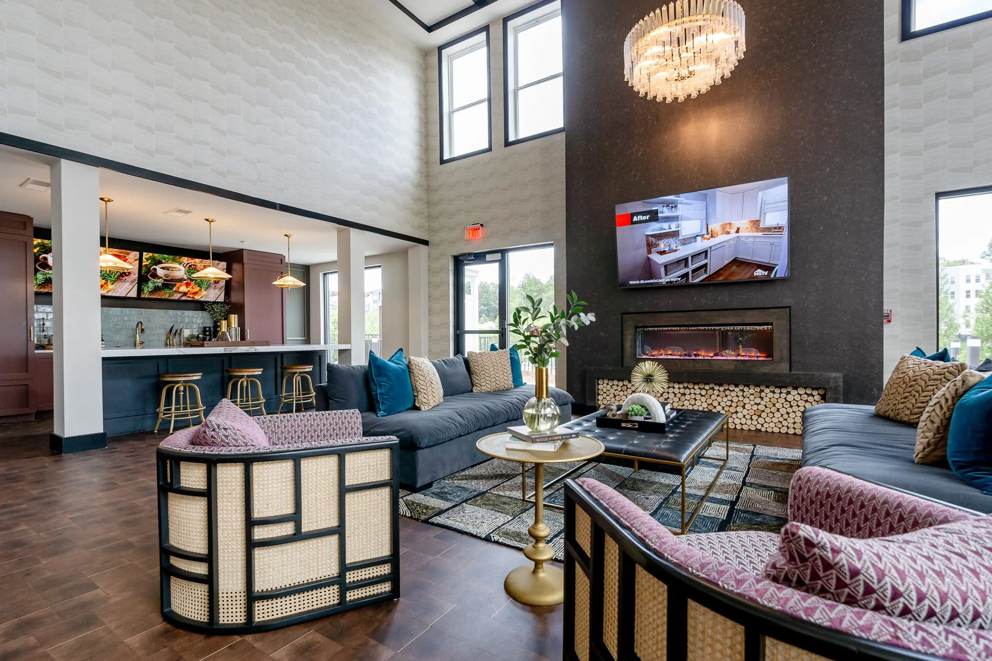 Multifamily amenity fireplace lounge with cane armchairs and navy sofas, a crystal chandelier and the bar at left