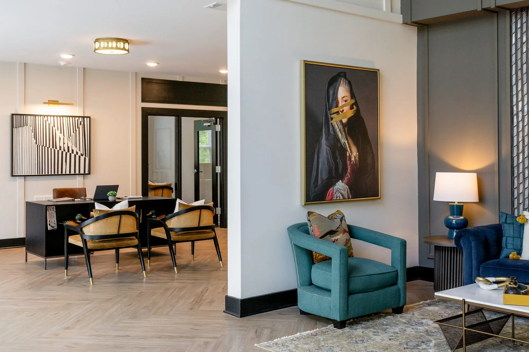 Multifamily amenity lobby with a teal armchair under the veiled portrait, the leasing desk and a black and white abstract
