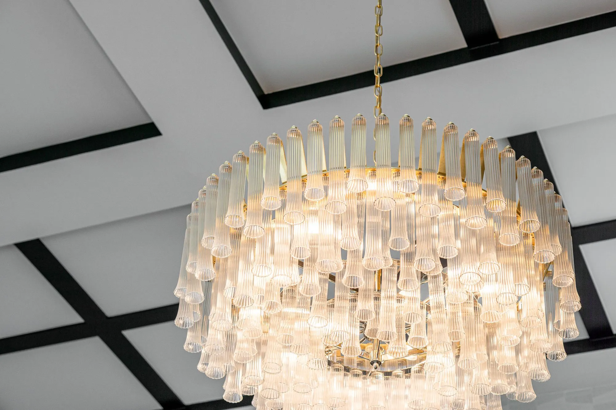 Multifamily amenity clubroom with a crystal rod chandelier against a white ceiling of black grid beams