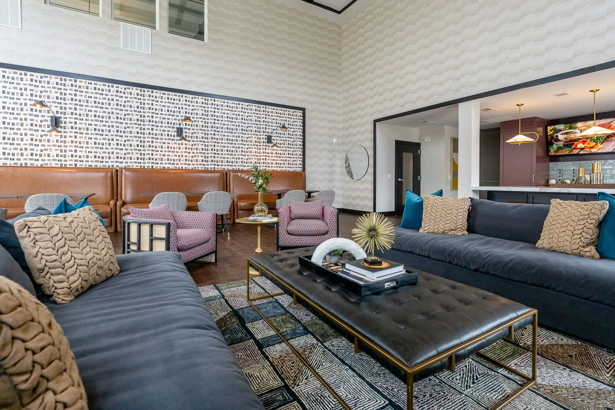 Multifamily amenity clubroom past navy sofas and a tufted ottoman to the booths and the mauve bar beyond