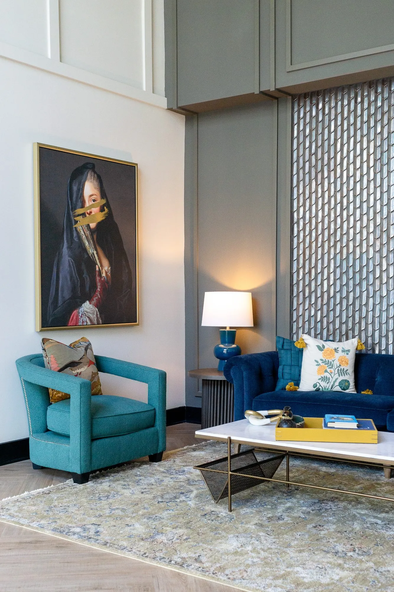 Multifamily amenity lobby seating corner, the veiled portrait above a teal chair beside a navy sofa and tall tile panel