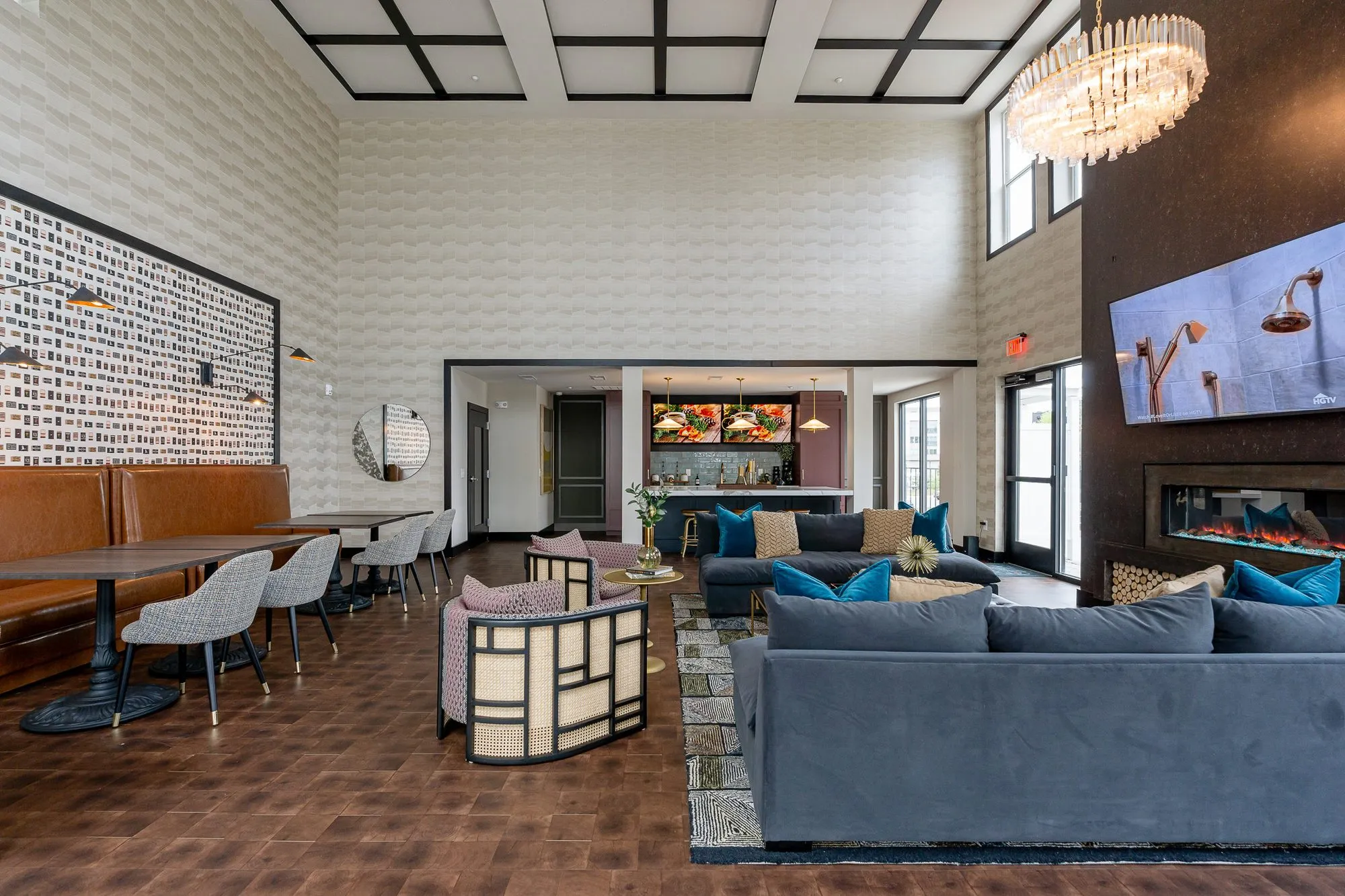 Multifamily amenity clubroom with leather booths and grey chairs at left, navy sofas facing the fireplace wall and screen