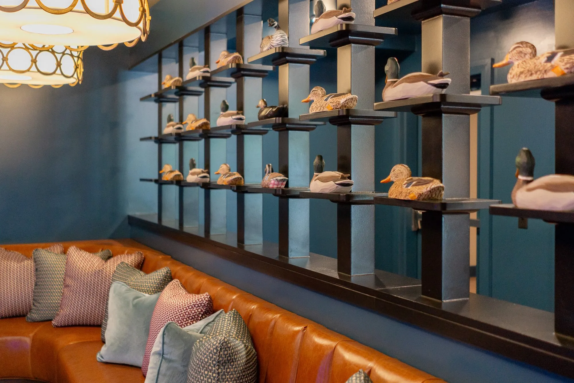 Multifamily amenity bowling lounge with a shelving wall of carved duck decoys above a cognac banquette and pillows