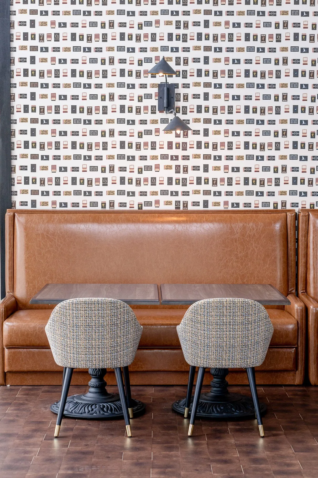 Multifamily amenity clubroom with a leather booth and two grey woven chairs at a table below matchbook wallpaper