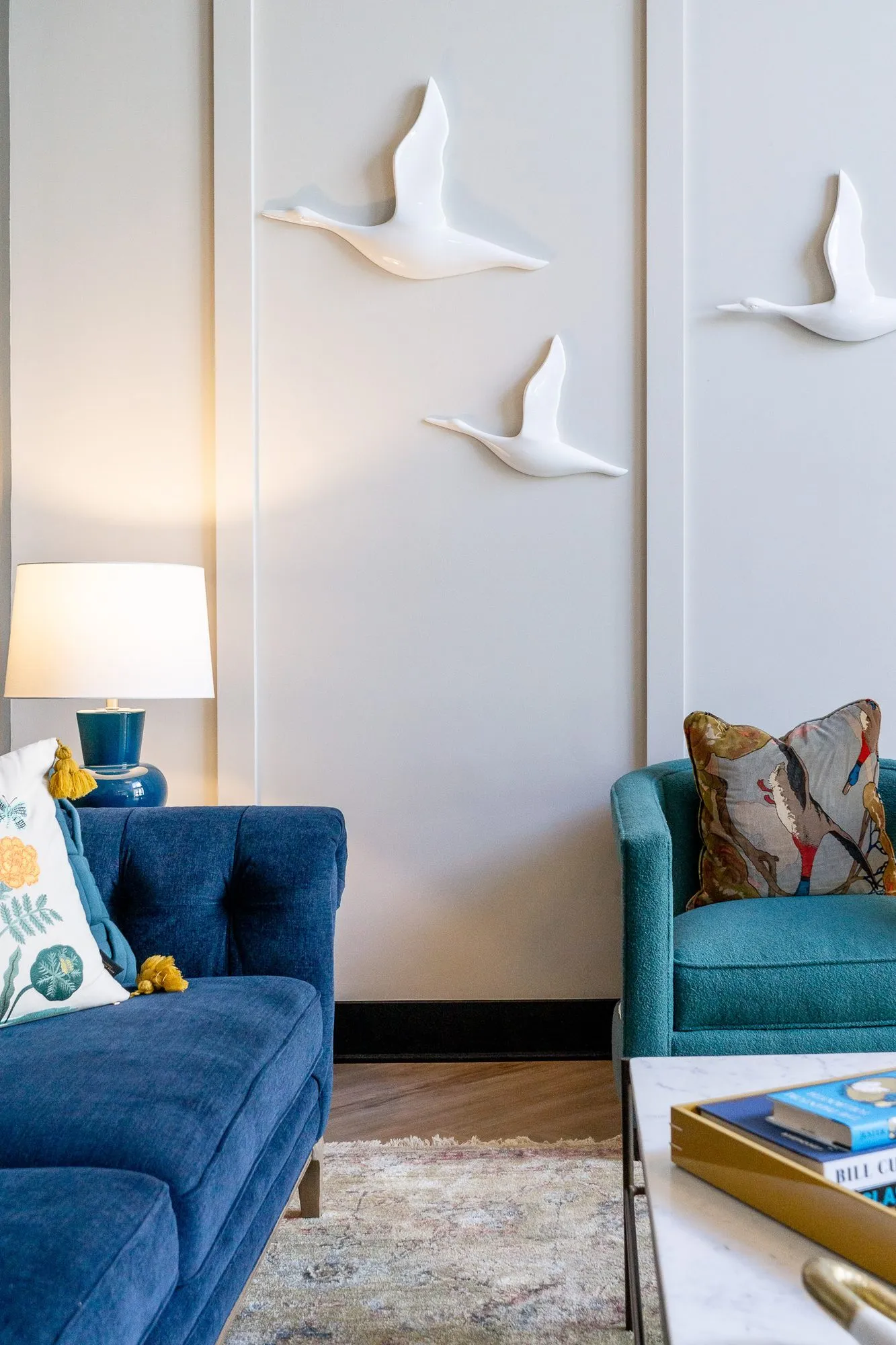 Multifamily amenity lobby lounge with white bird sculptures above a navy sofa and teal armchair