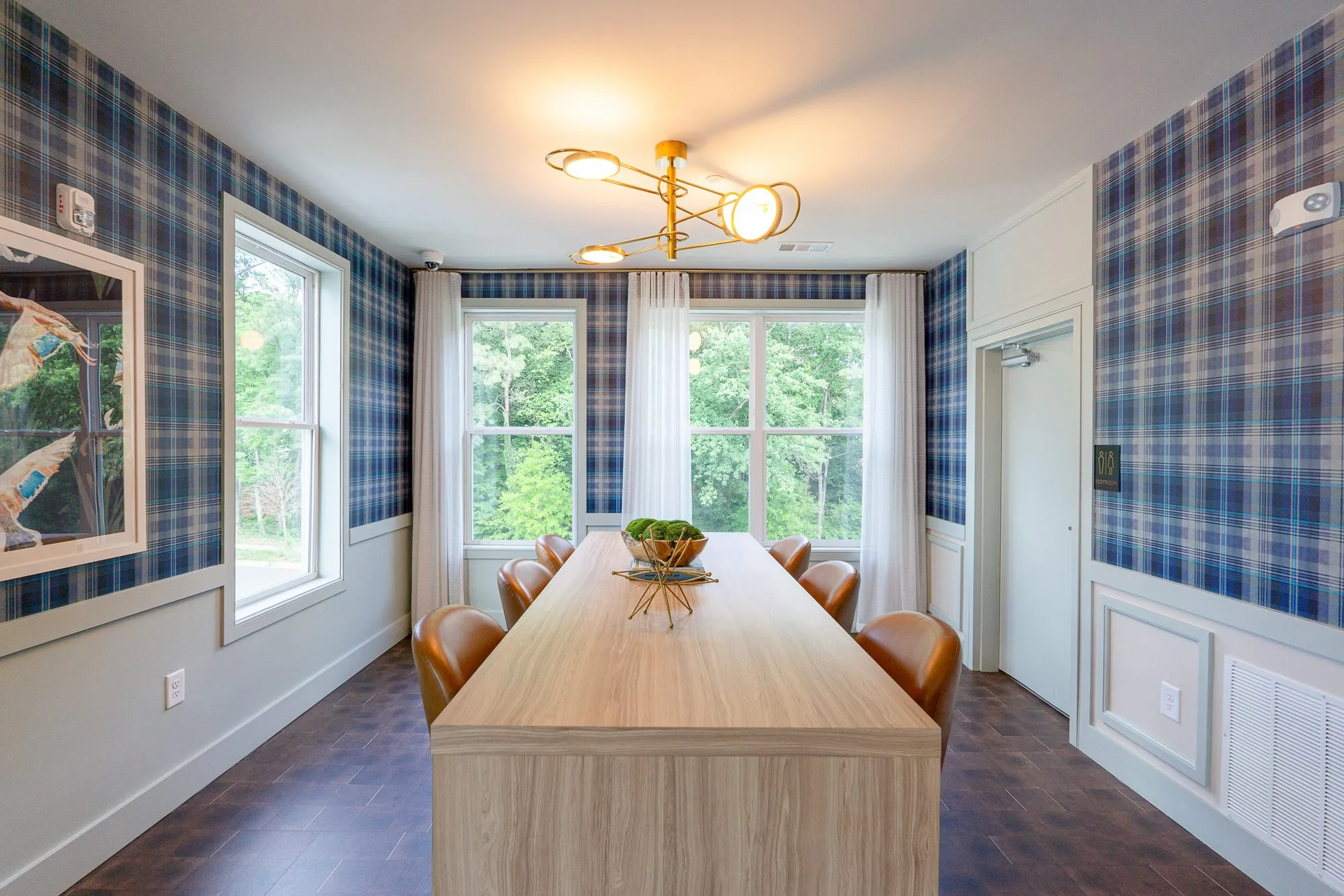 Multifamily amenity conference room with blue plaid walls, a long pale wood table and cognac chairs by curtained windows