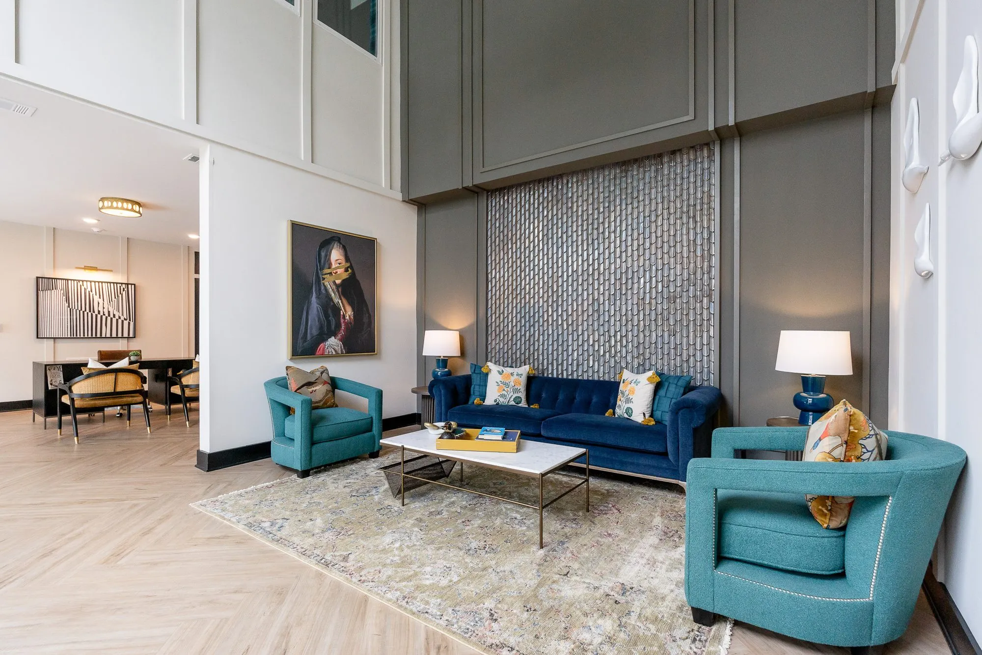 Multifamily amenity lobby lounge corner with teal chairs, navy sofa and tile panel, the leasing area at left