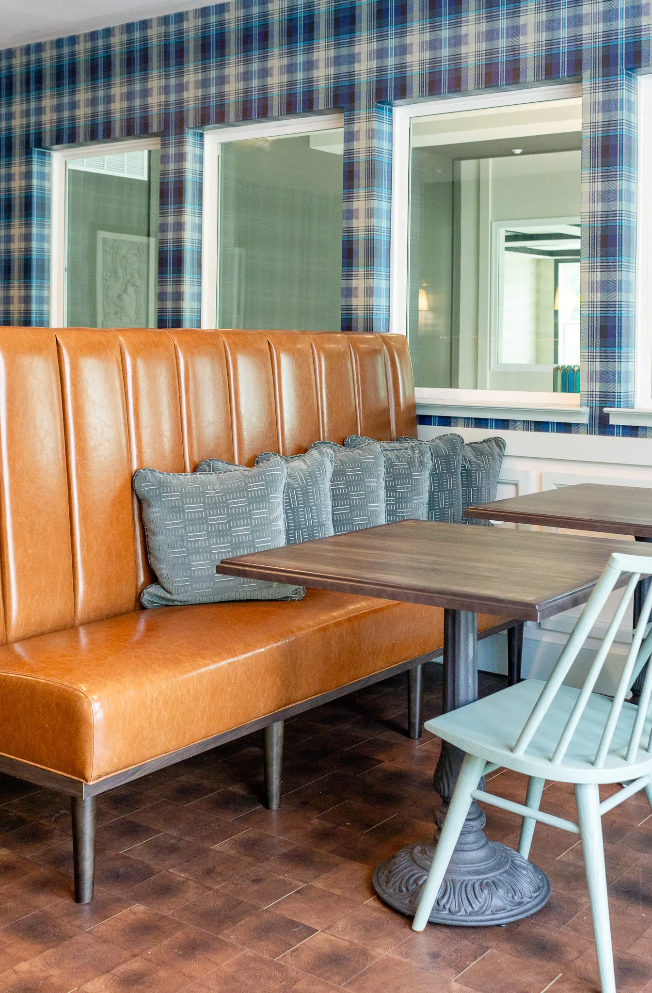 Multifamily amenity cafe banquette, a tan leather bench and windsor chairs at wood tables against plaid wallcovering