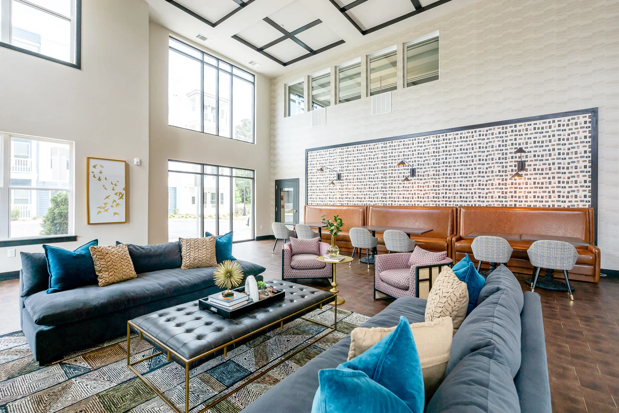 Multifamily amenity double height clubroom under a black gridded coffered ceiling, navy sofas and caramel banquettes