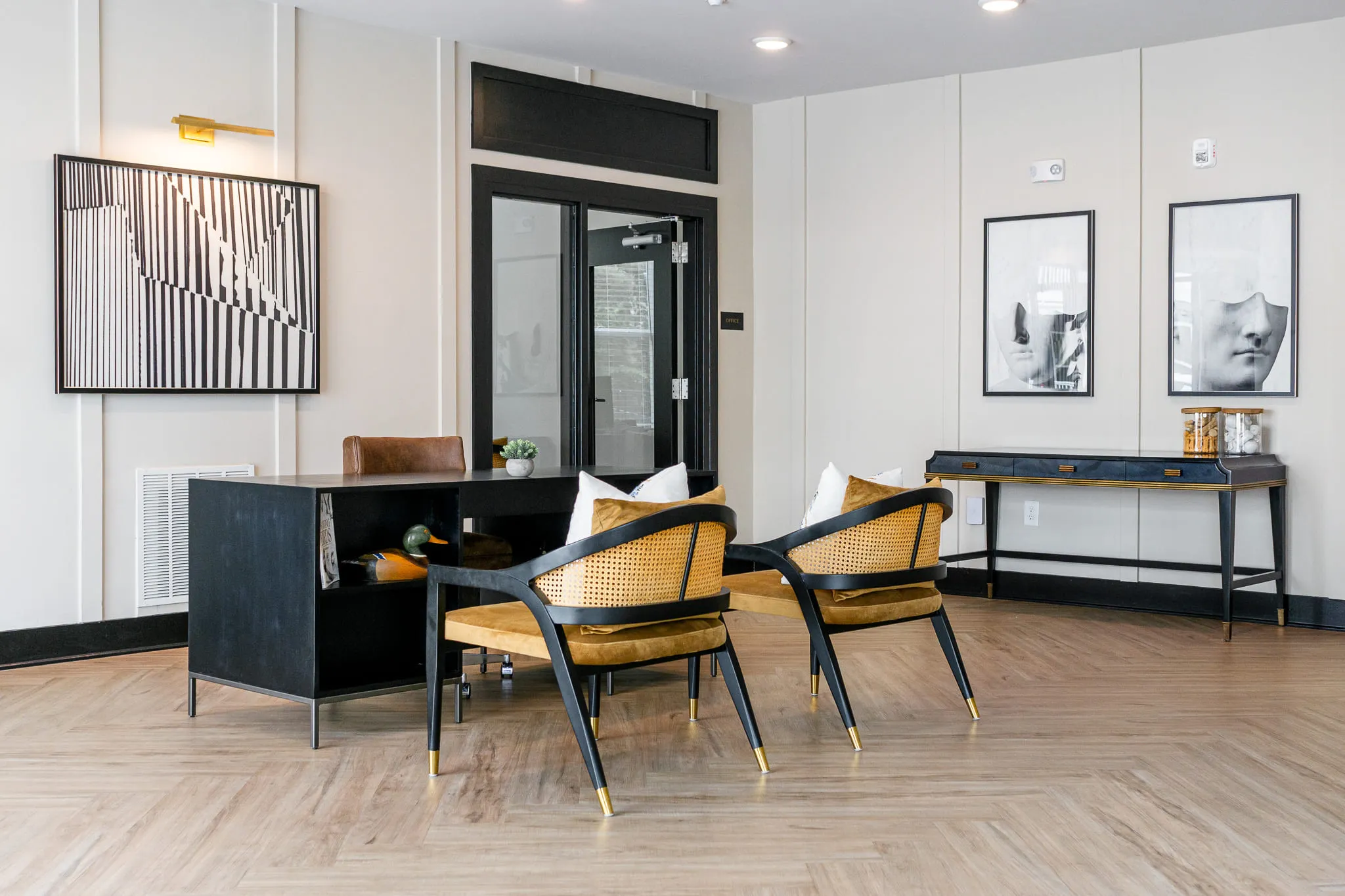 Multifamily amenity leasing office with a black desk and caned chairs between framed black and white prints