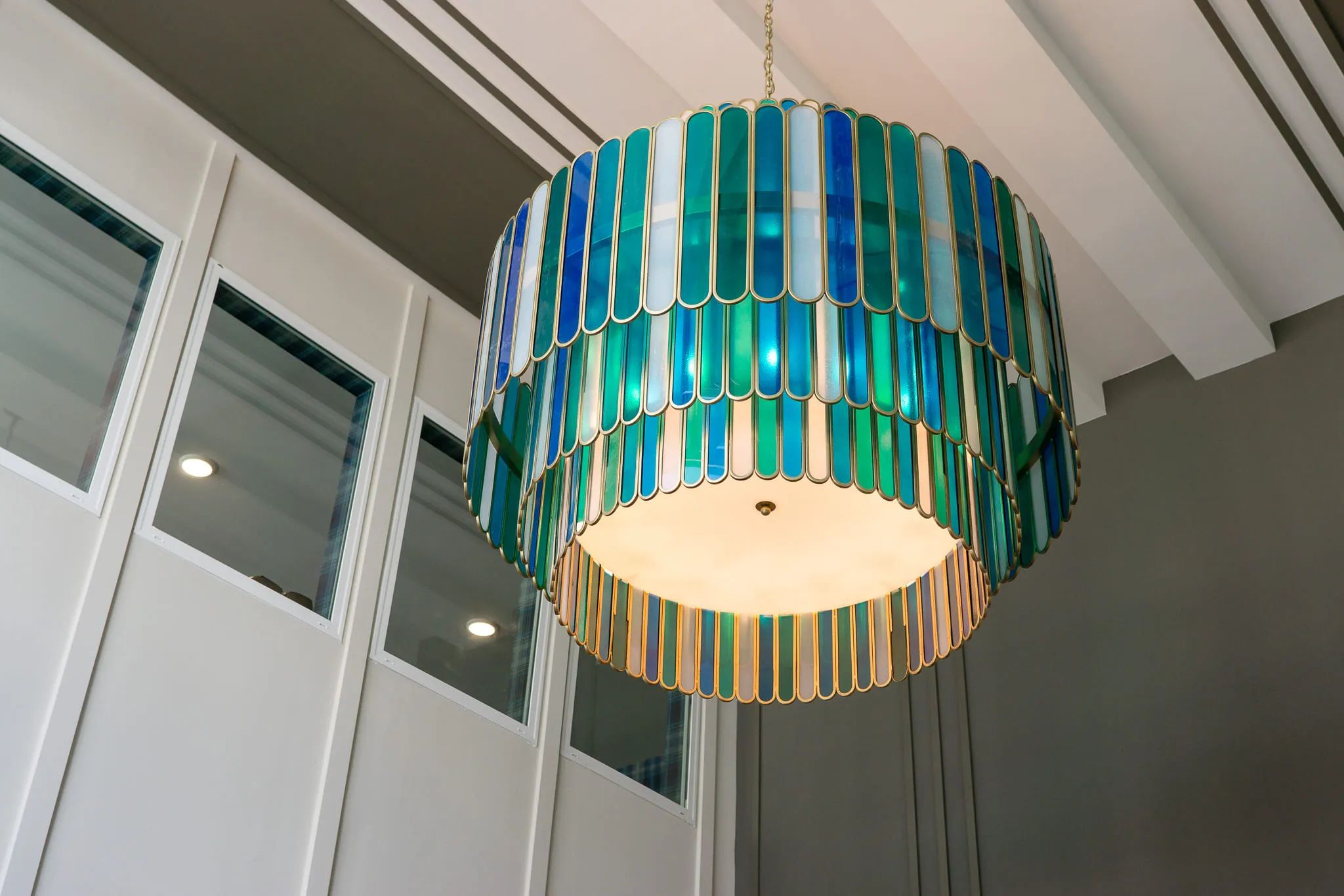 Multifamily amenity interior detail: tiered chandelier of blue and green glass fins below a white beamed ceiling