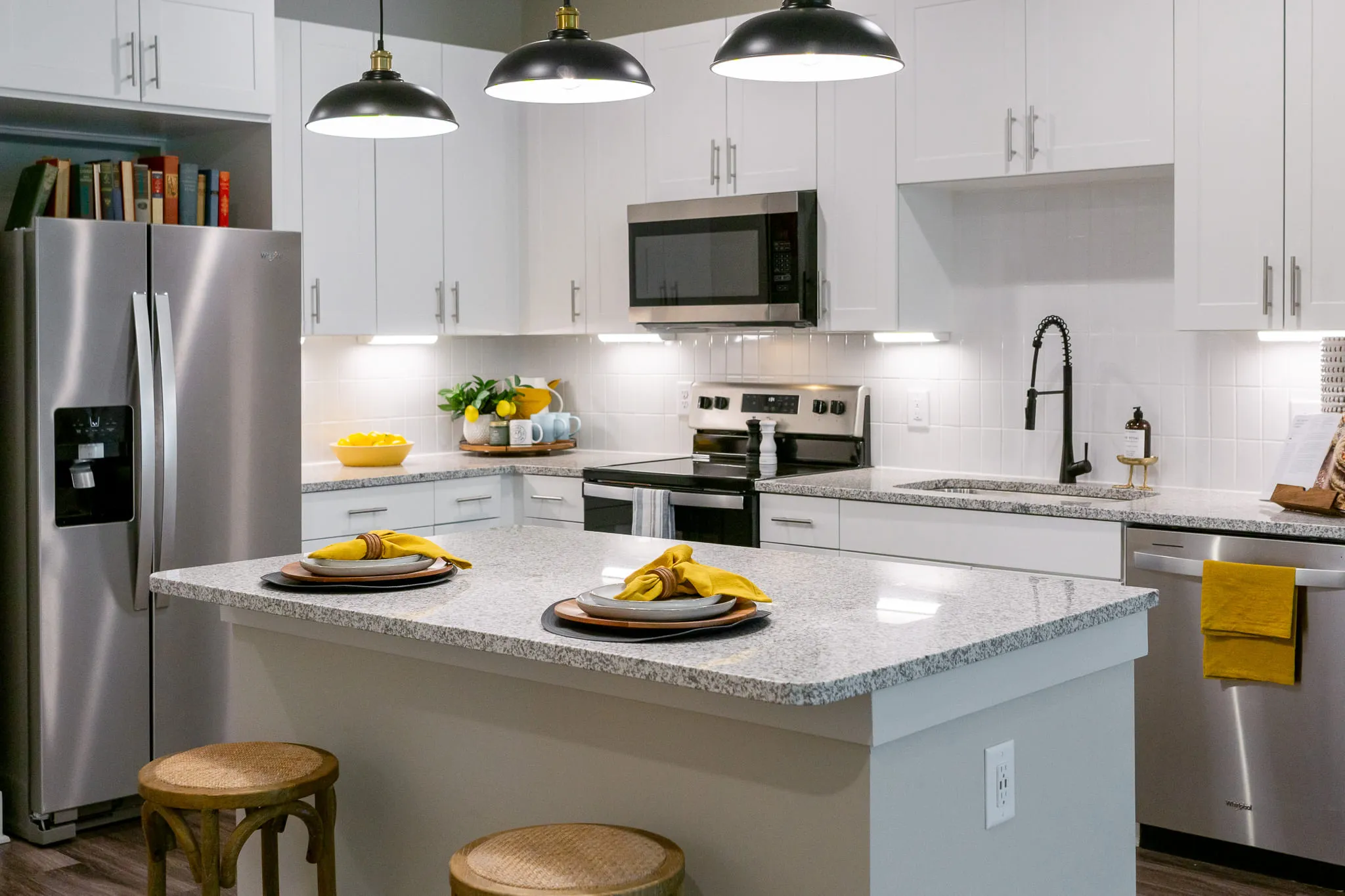 Multifamily apartment model kitchen with white cabinetry and a granite island with wood counter stools under black pendants