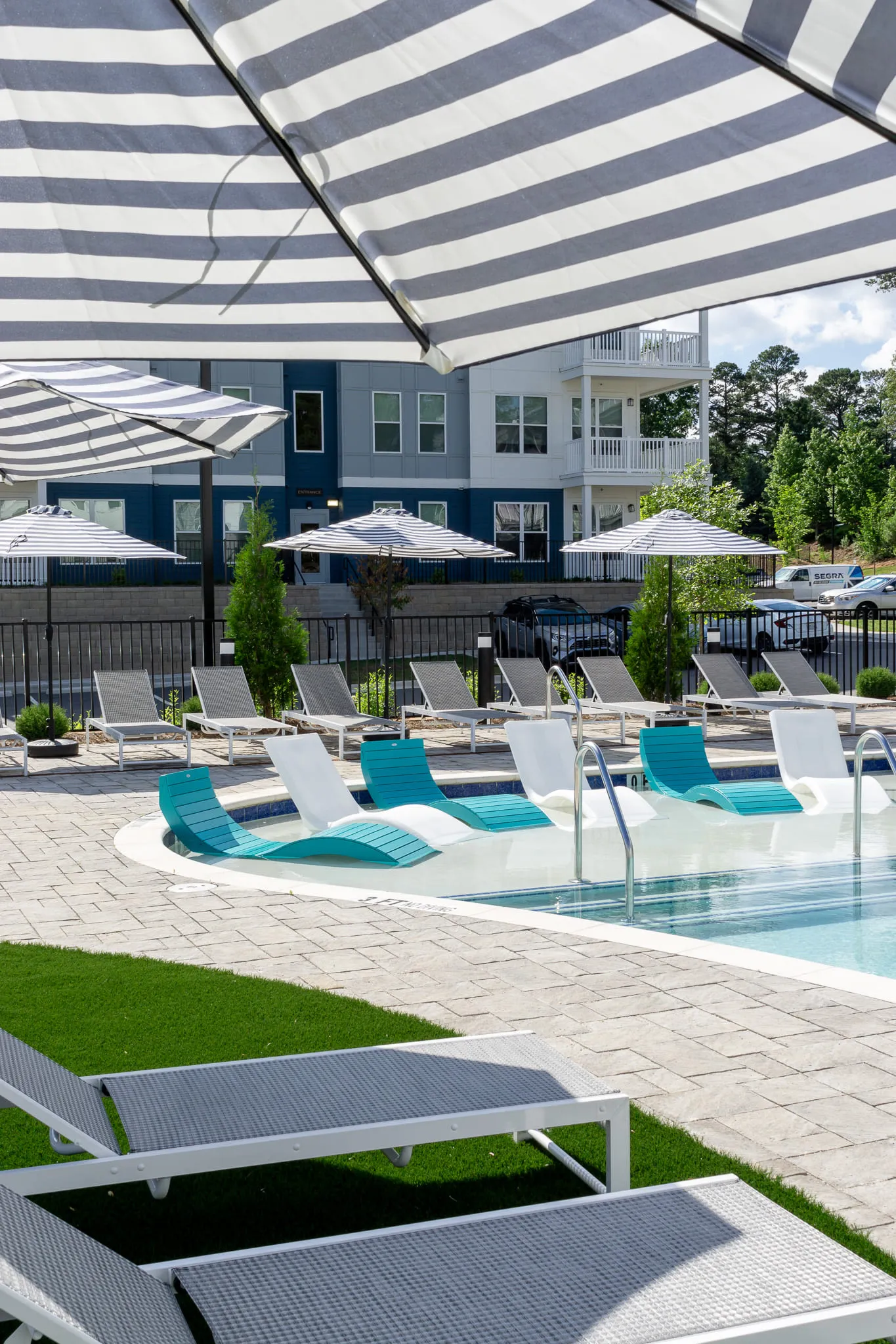 Multifamily community pool with teal chaises and striped umbrellas along the deck in front of the residences