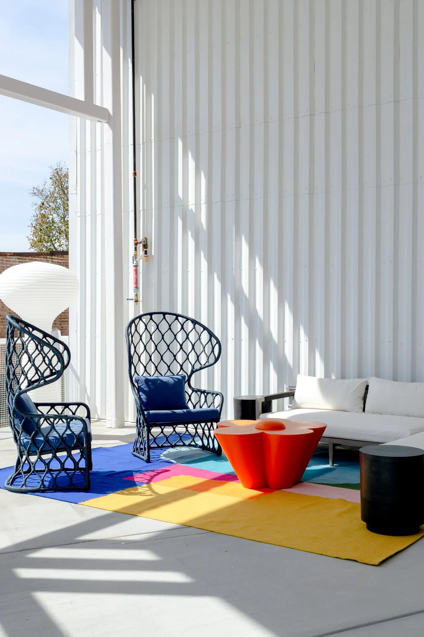 Multifamily community terrace with navy peacock chairs and an orange table on a colour-block rug by fluted metal cladding