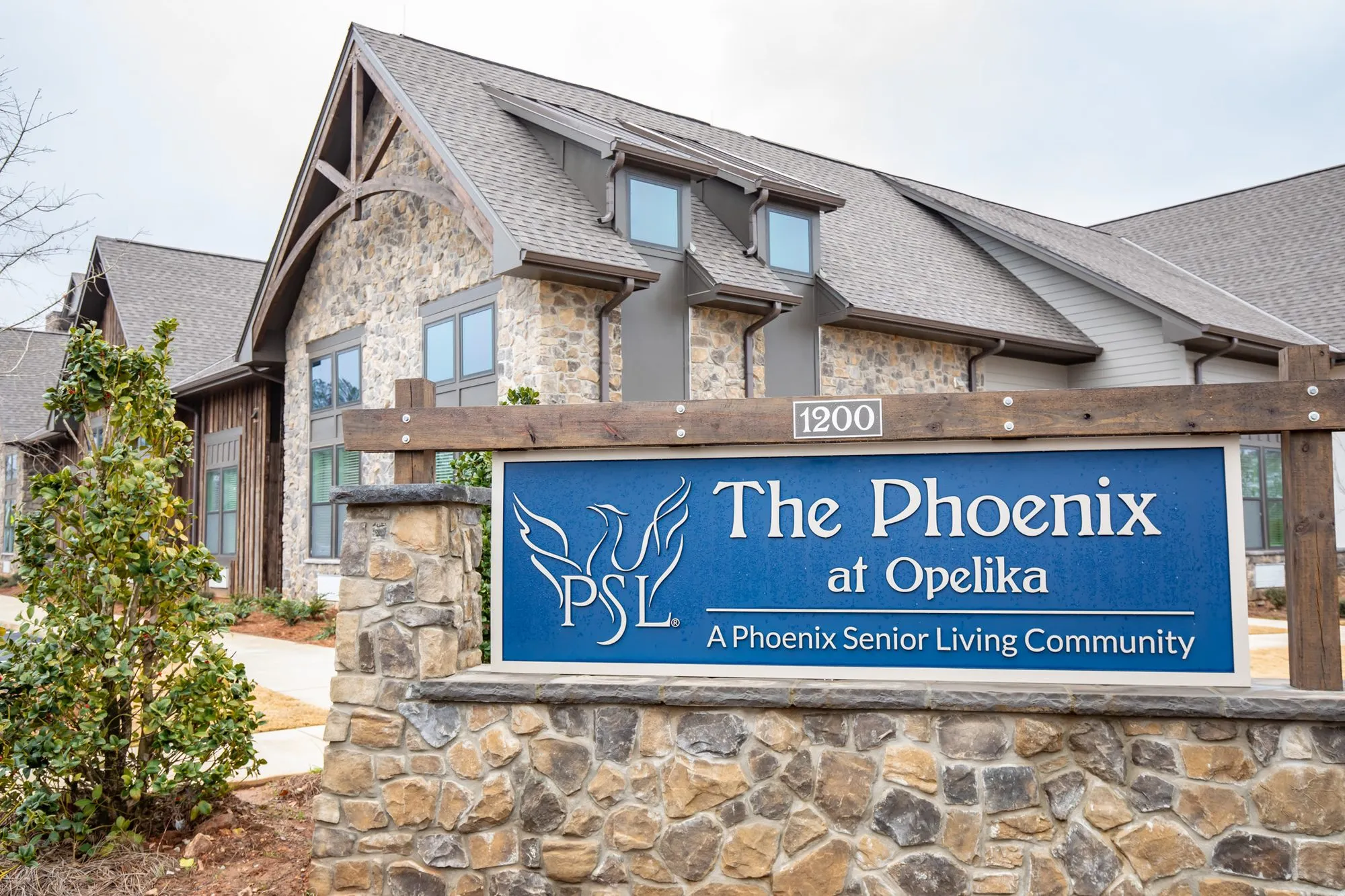 Senior living community exterior: monument sign on its stone base, a magnolia beside it and the stone facade behind