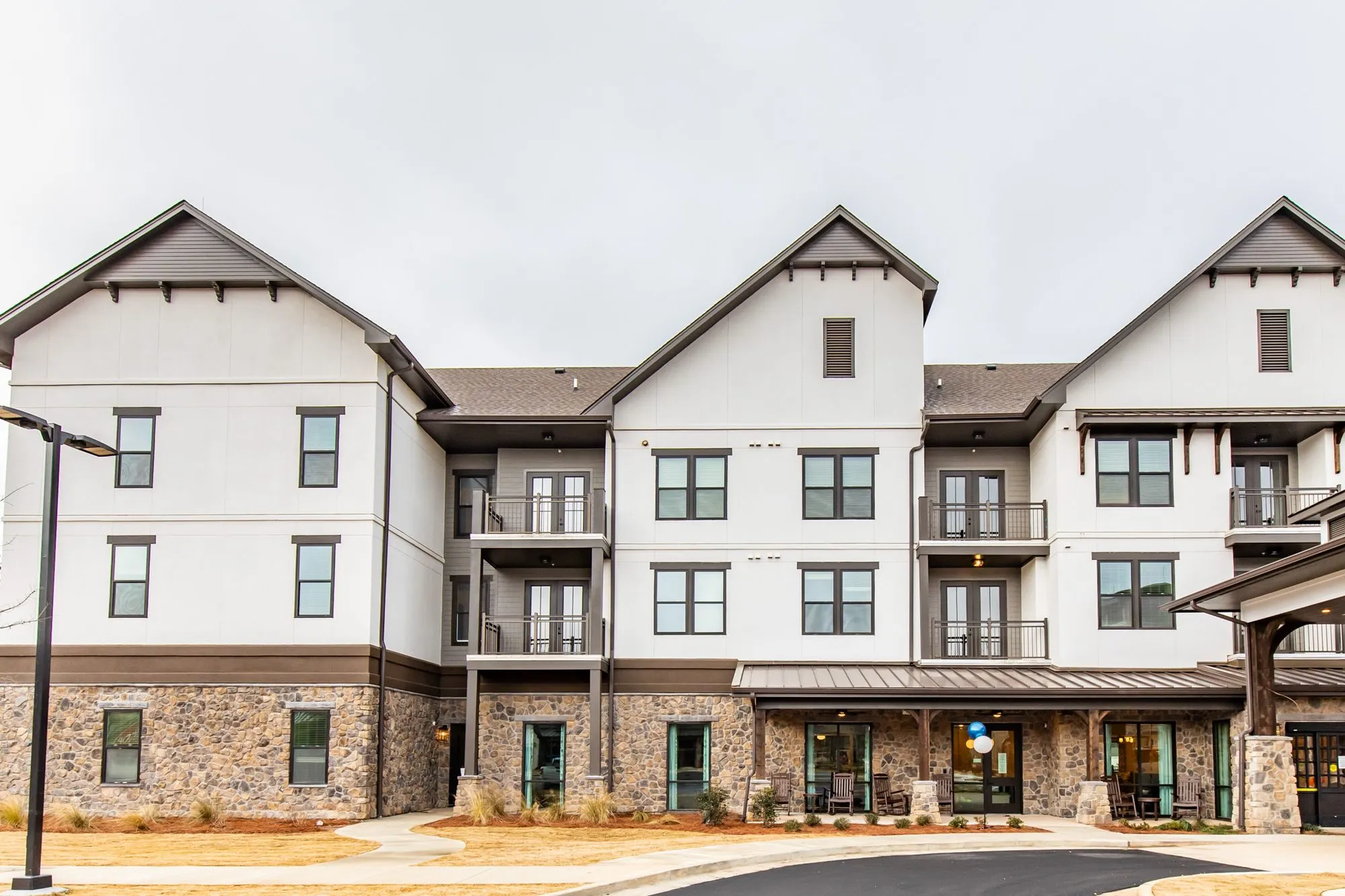 Senior living community exterior: three storey building with white upper floors, a stone base, balconies and gables
